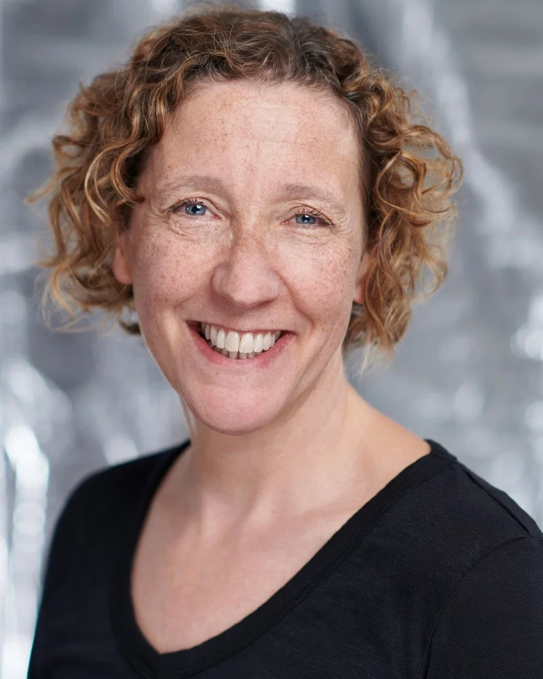 Jessie Cunnett, a woman with curly hair, smiles at the camera against a silver background.