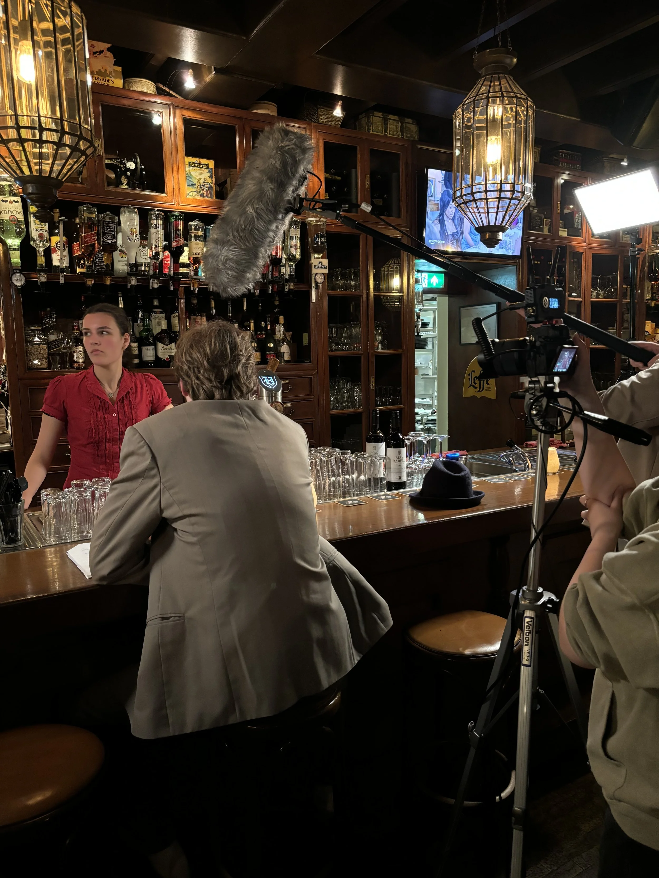 Video opname in bar met twee mensen aan de bar en een camera met microfoon, filmopname voor een programma.