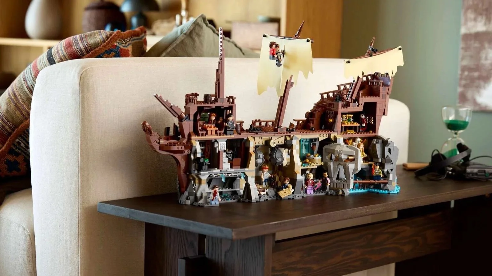 The Goonies LEGO set with its pirate ship and skull cave displayed on a dark wood console table behind a cream sofa.