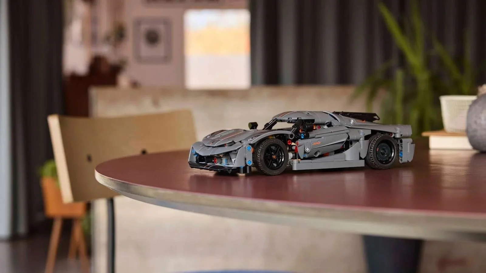 LEGO Technic Koenigsegg Jesko Absolut hypercar in gray with orange accents, displayed on a round wooden table with a blue stool nearby