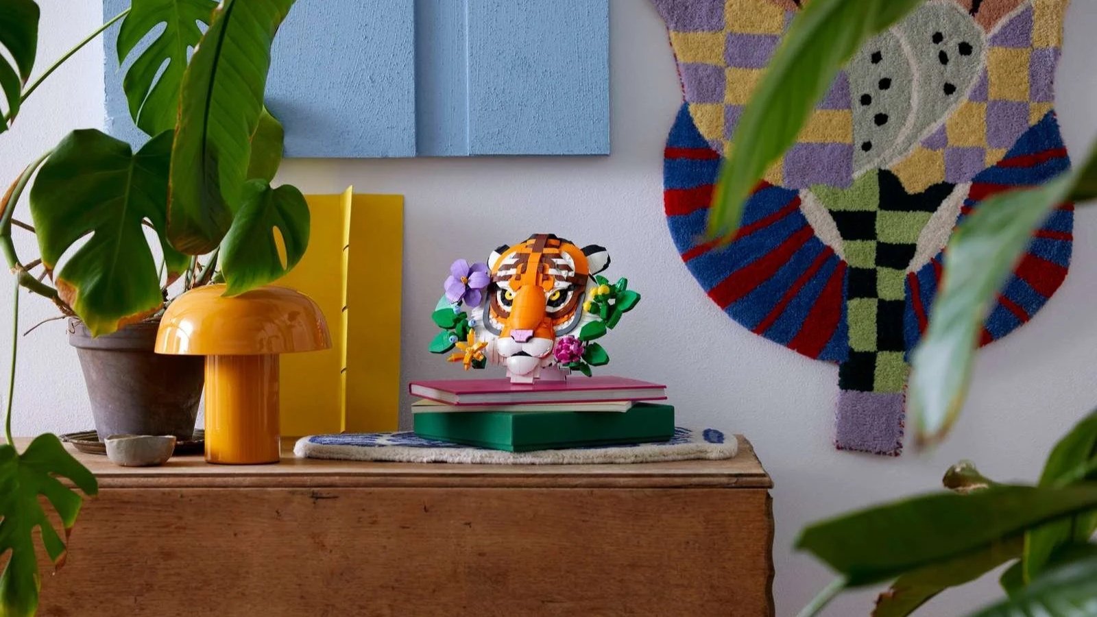 LEGO Fauna Collection tiger head with flowers displayed on stacked books atop a wooden sideboard beside a monstera plant