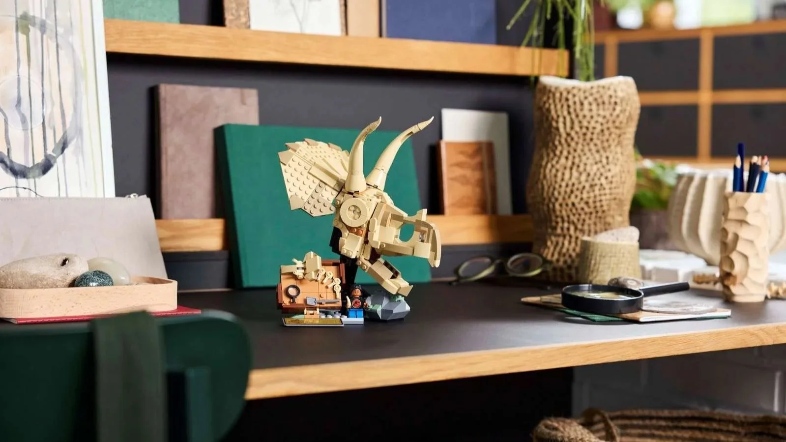 LEGO Dinosaur Fossils Triceratops skull in tan bricks with a fossil dig scene, displayed on a dark desk with a magnifying glass