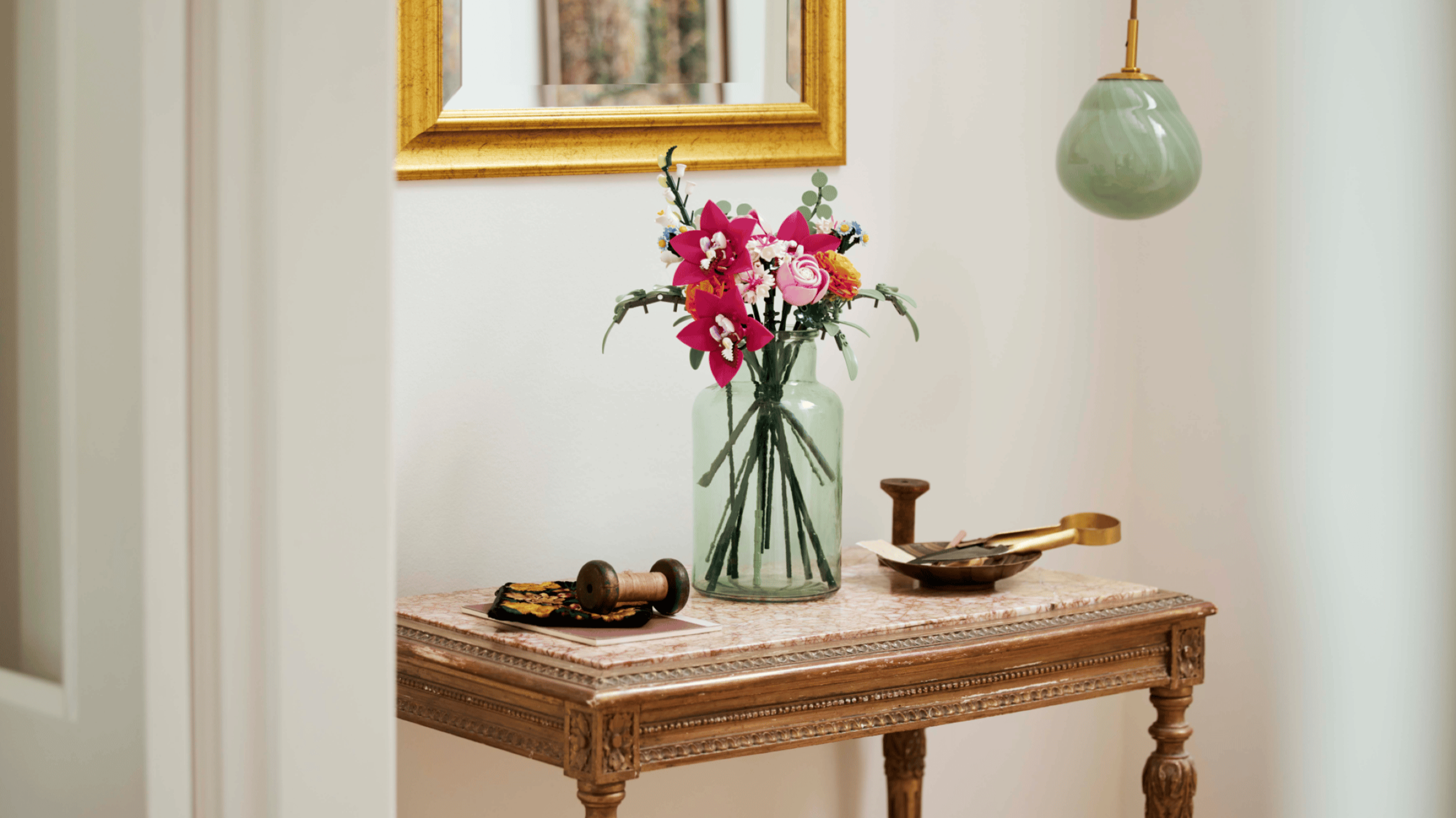 LEGO Pretty Pink Flower Bouquet set in a glass jar on an antique marble-top table, beneath a gilt mirror and a hanging pendant light
