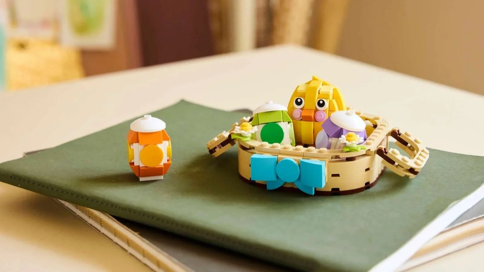 LEGO Easter Egg Basket set on a green notebook, with a yellow chick and pastel eggs in a tan basket with a blue bow, plus one loose orange egg