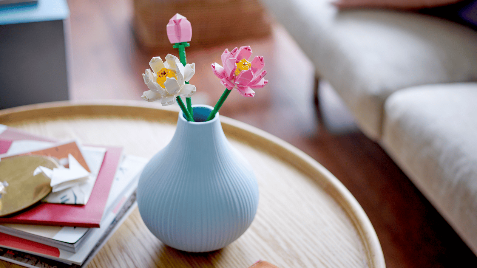 Pink and white LEGO Lotus Flowers in a pale blue vase on a round wooden coffee table