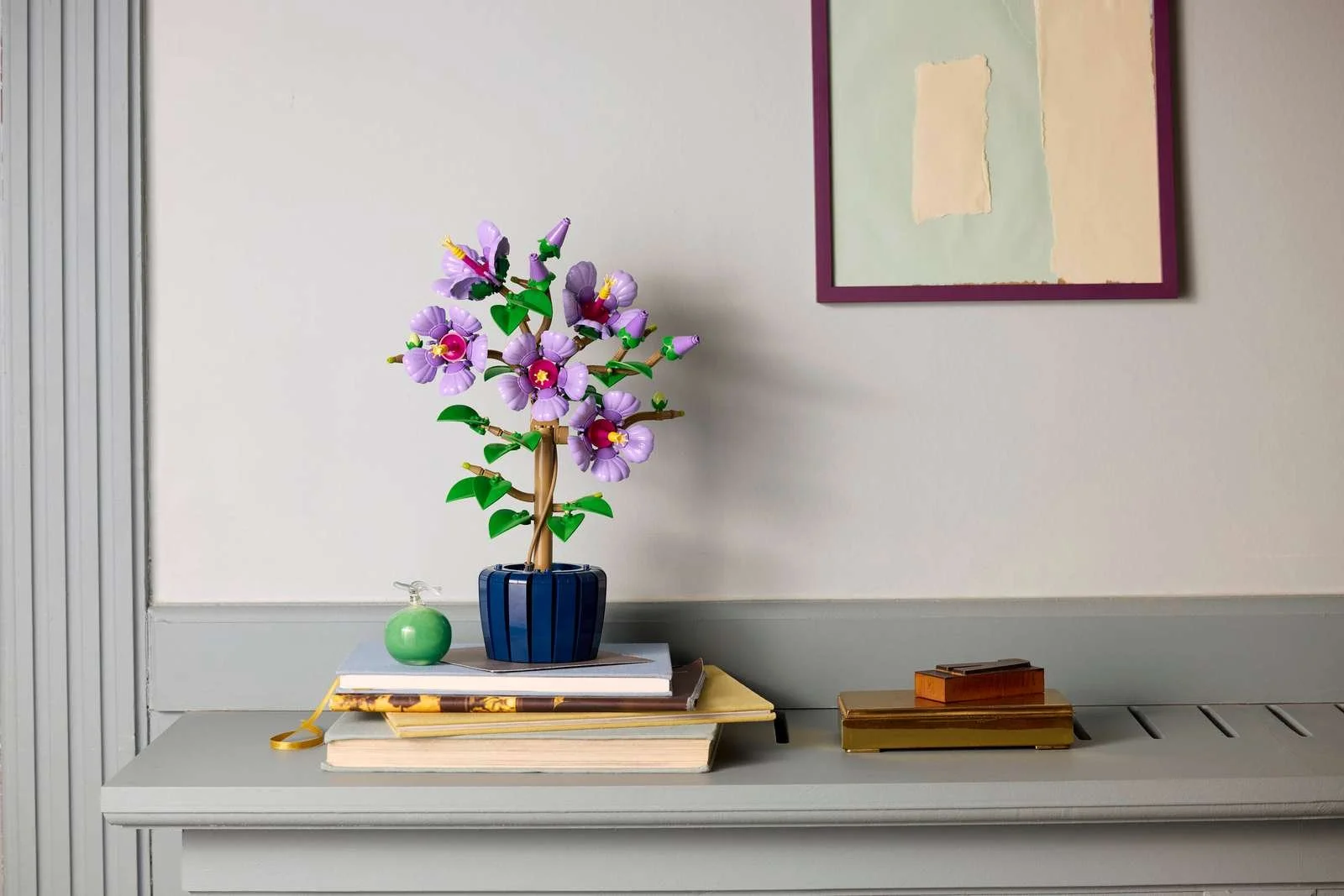 Purple LEGO Hibiscus flowers styled as shelf decor beside a framed print and vintage books