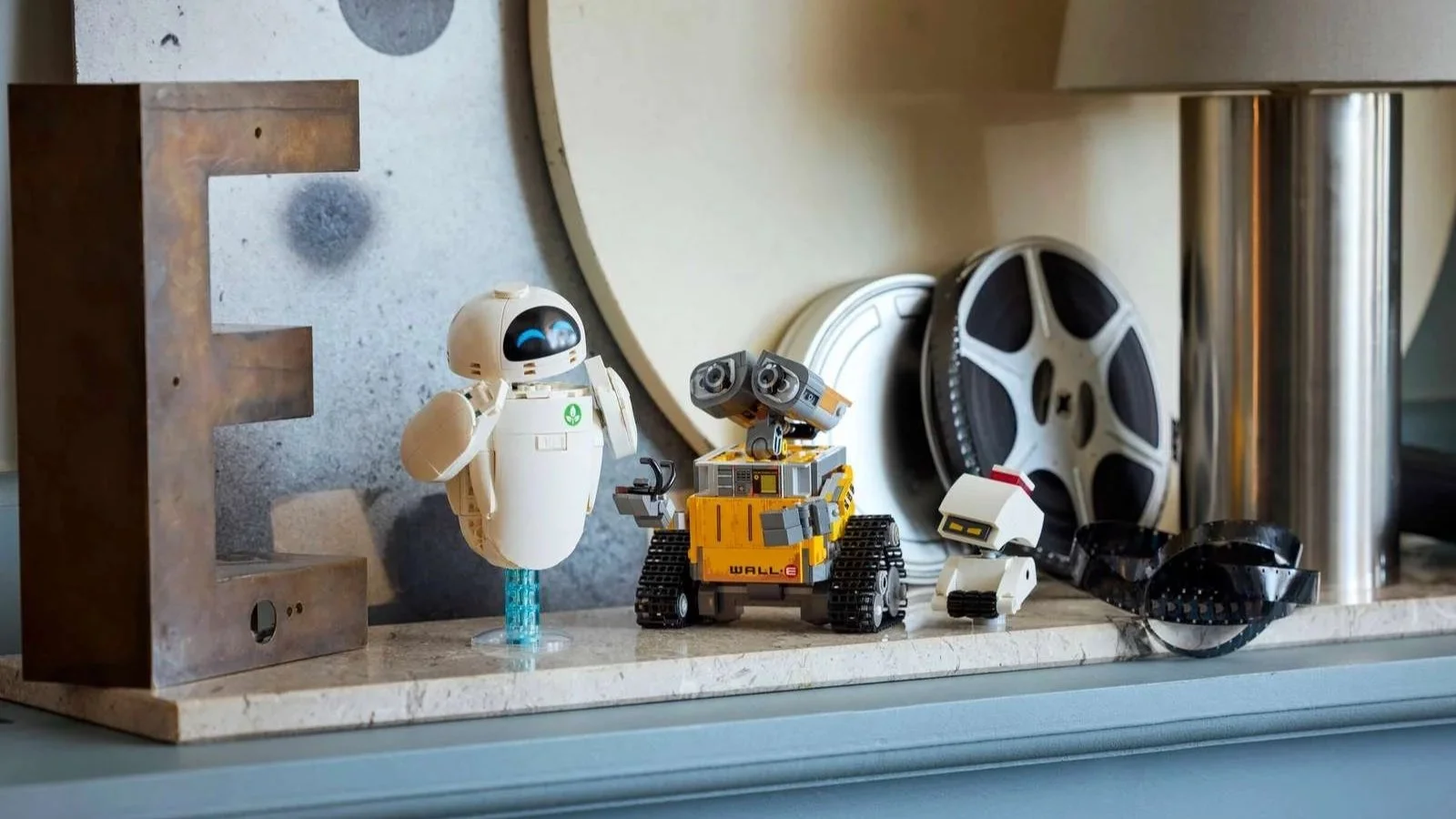 LEGO WALL-E and EVE set displayed on a marble countertop between vintage film reels and a metal letter
