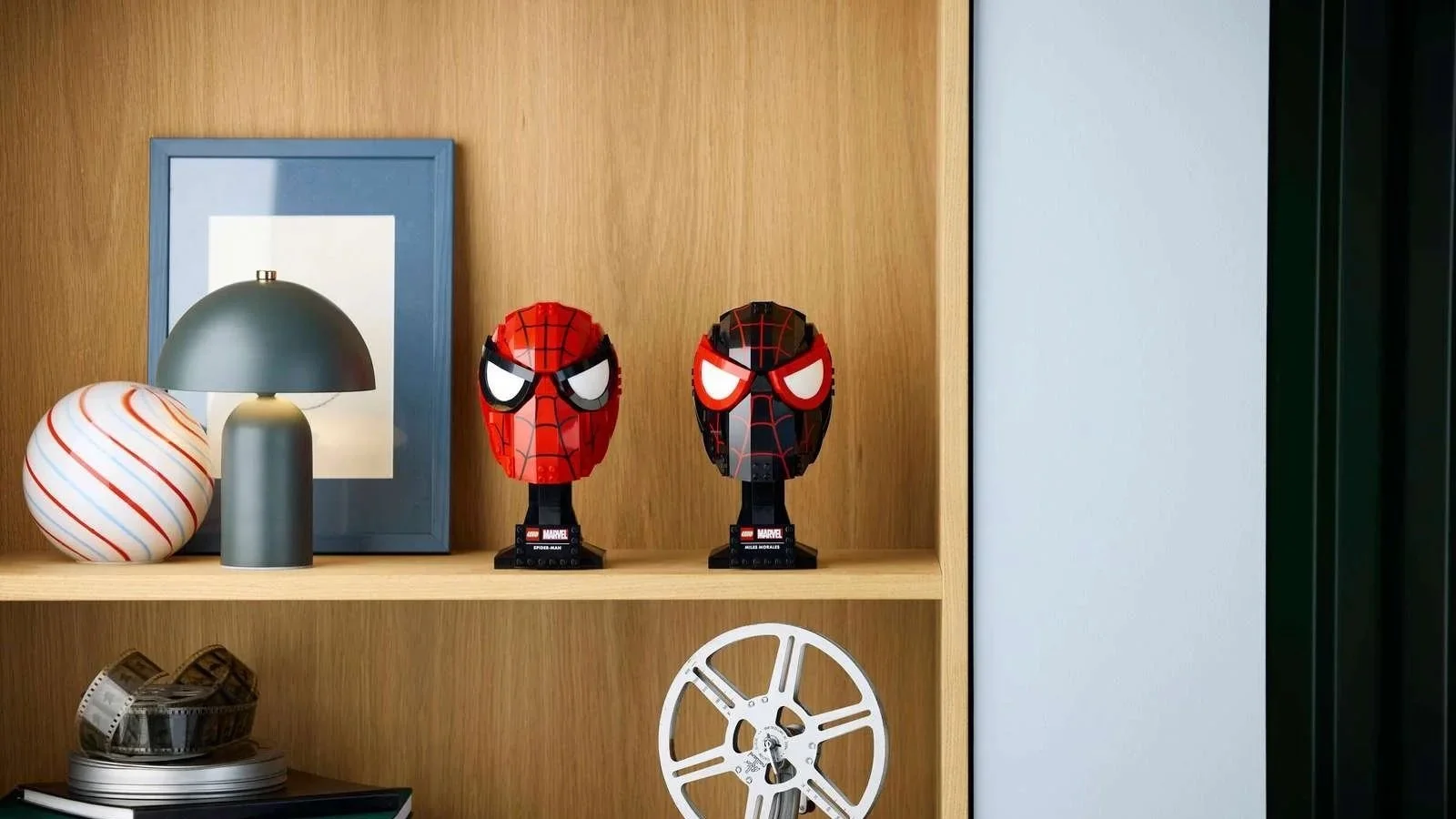 LEGO Marvel Peter Parker's & Miles Morales' Masks standing side by side on an oak bookshelf next to a green lamp