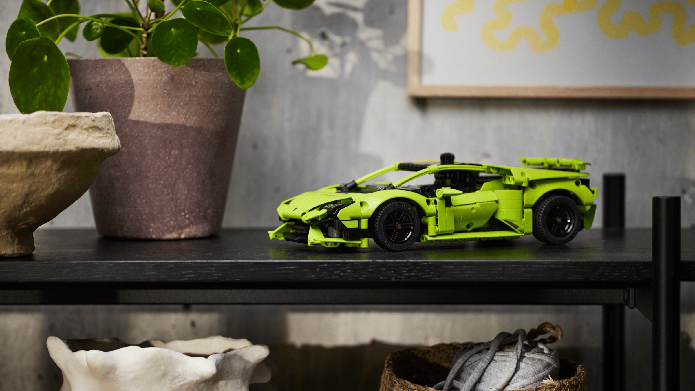 LEGO Technic Lamborghini Huracán Tecnica model car in lime green with black accents, displayed on a black shelf beside a potted plant