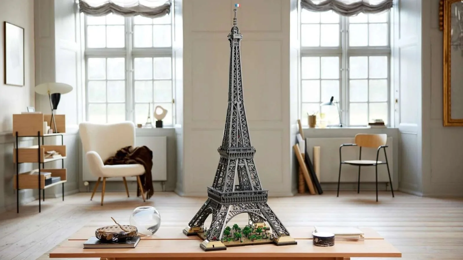 LEGO Eiffel Tower model with a French flag on top, displayed on a wooden table in a bright room with tall windows