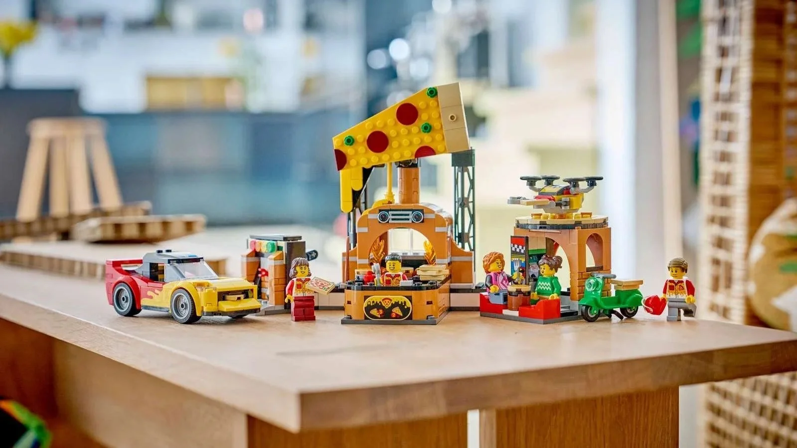 LEGO Pizza Delivery Experience with Vehicles set with a giant pizza slice sign, a flame-decorated yellow car, a green scooter and a delivery drone on a wooden table