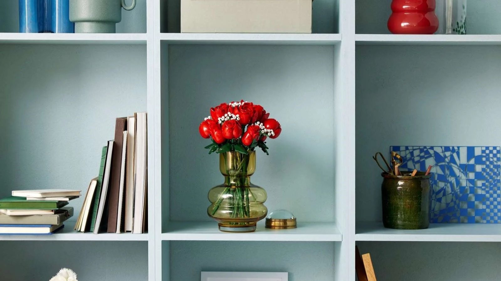 LEGO Bouquet of Roses set with red roses in an amber glass vase at the center of a light blue bookshelf