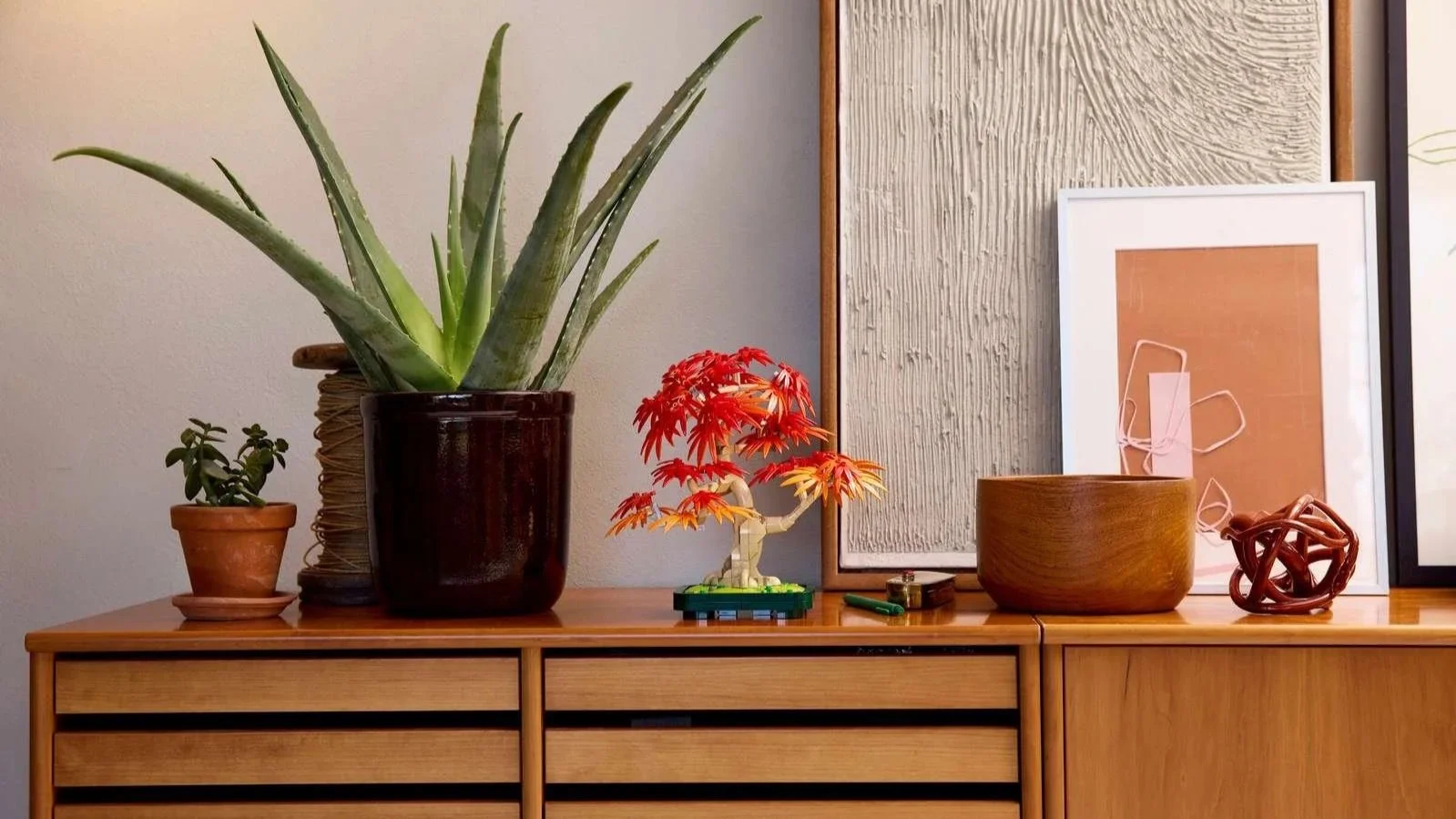 LEGO Japanese Red Maple Bonsai Tree in autumn color on a wooden dresser between an aloe plant and framed art