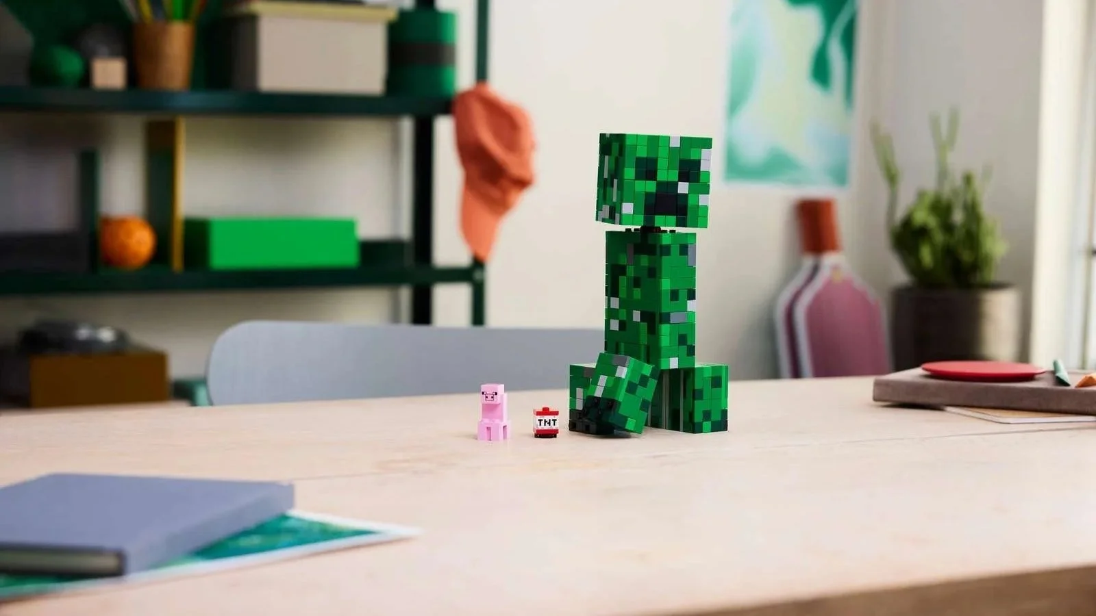 LEGO Minecraft Creeper figure on a desk beside a small pig and TNT figure, with shelving behind it