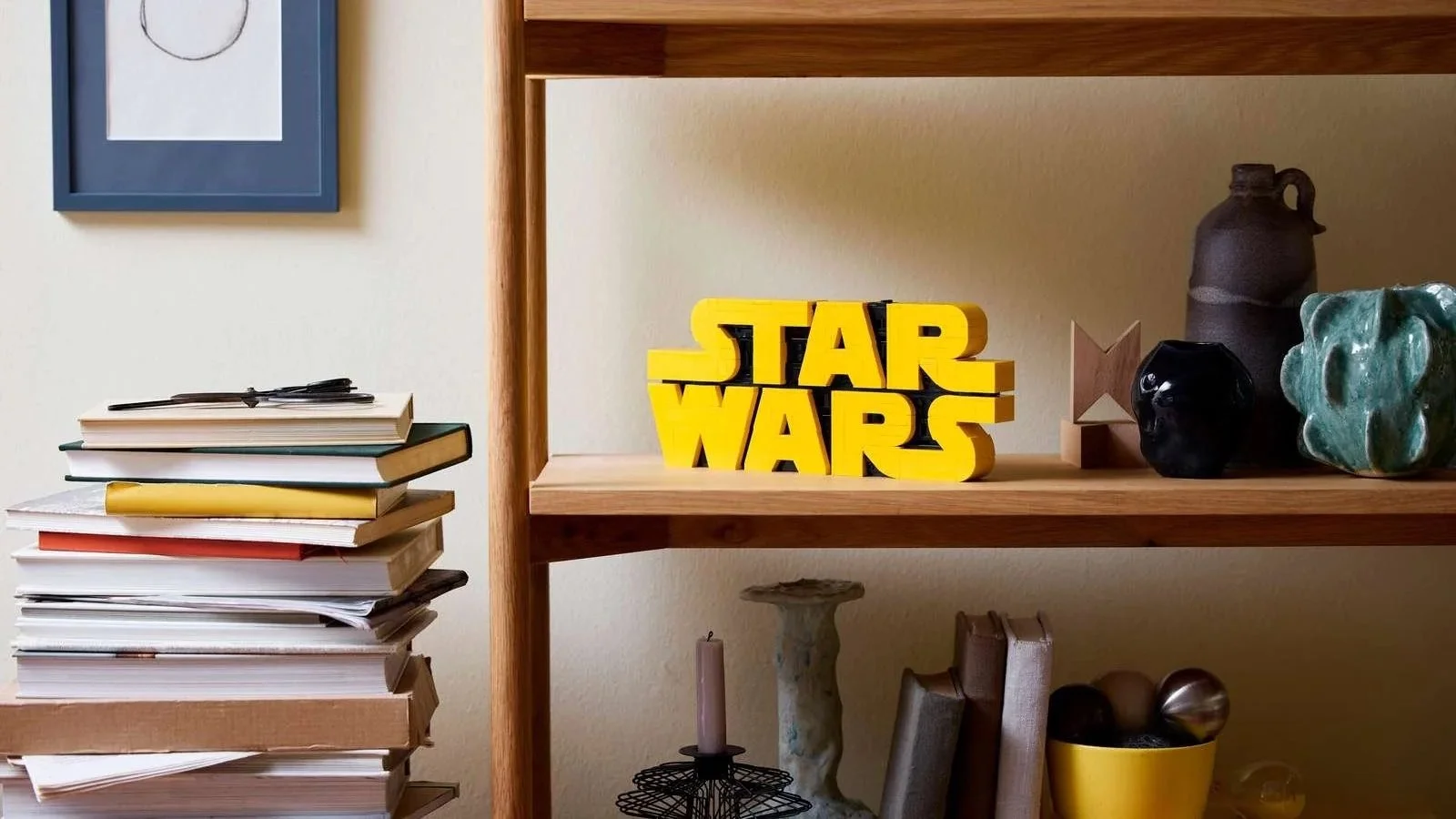 Yellow brick-built LEGO Star Wars logo styled on a wooden shelf between ceramics and a stack of art books