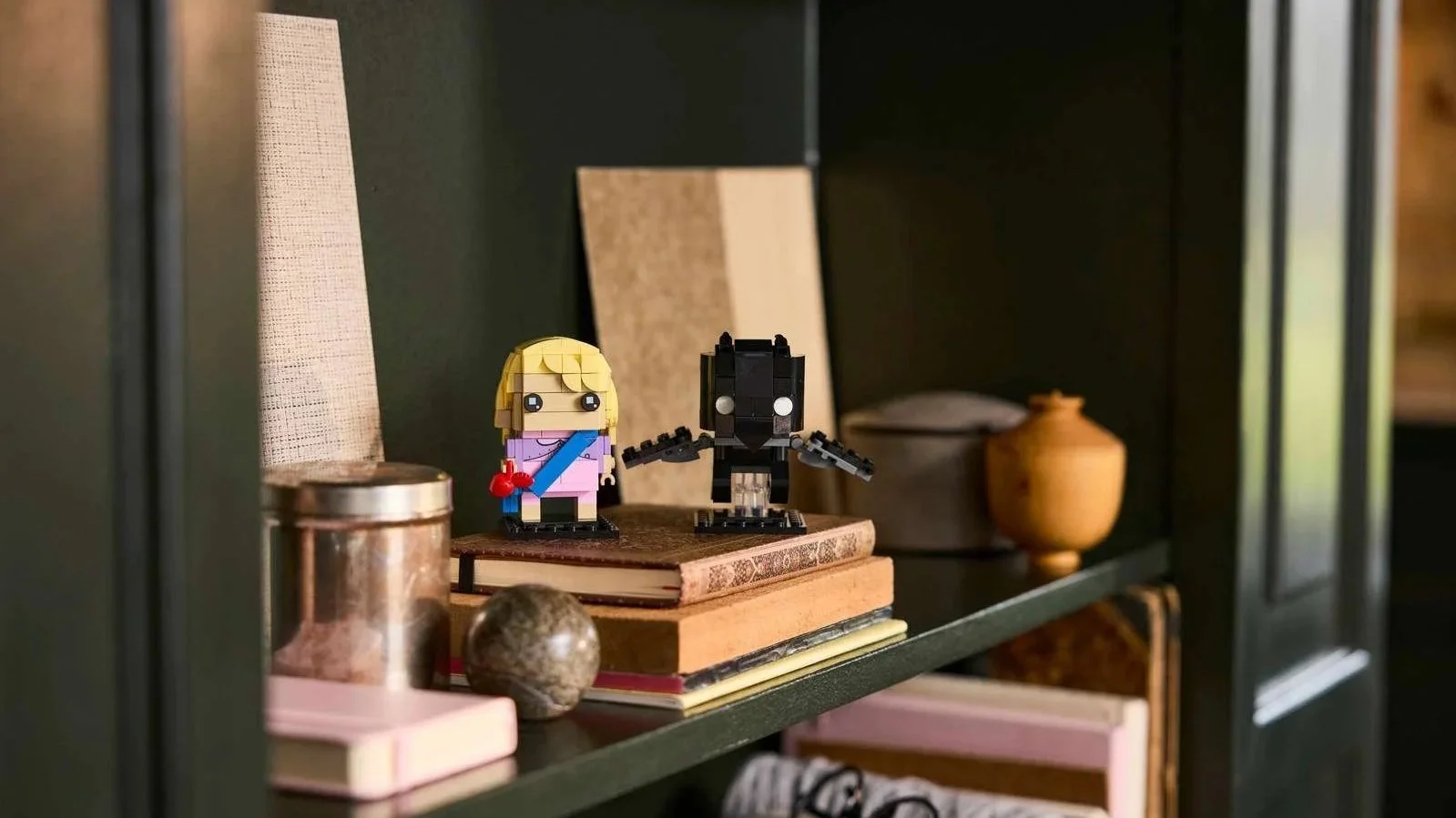 LEGO Luna Lovegood and Thestral figures with blocky heads on a dark green bookshelf next to vintage books and a stone sphere