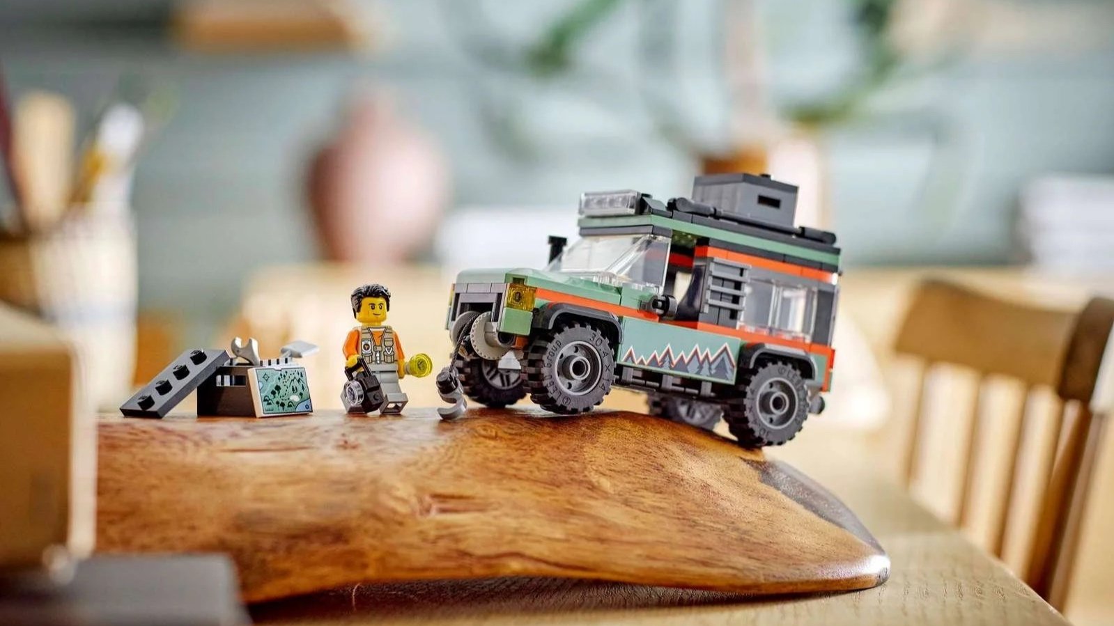 Off-Road 4x4 Mountain Truck LEGO set in green with orange stripes and a roof rack on a curved wooden board next to an explorer figure holding a camera and a map