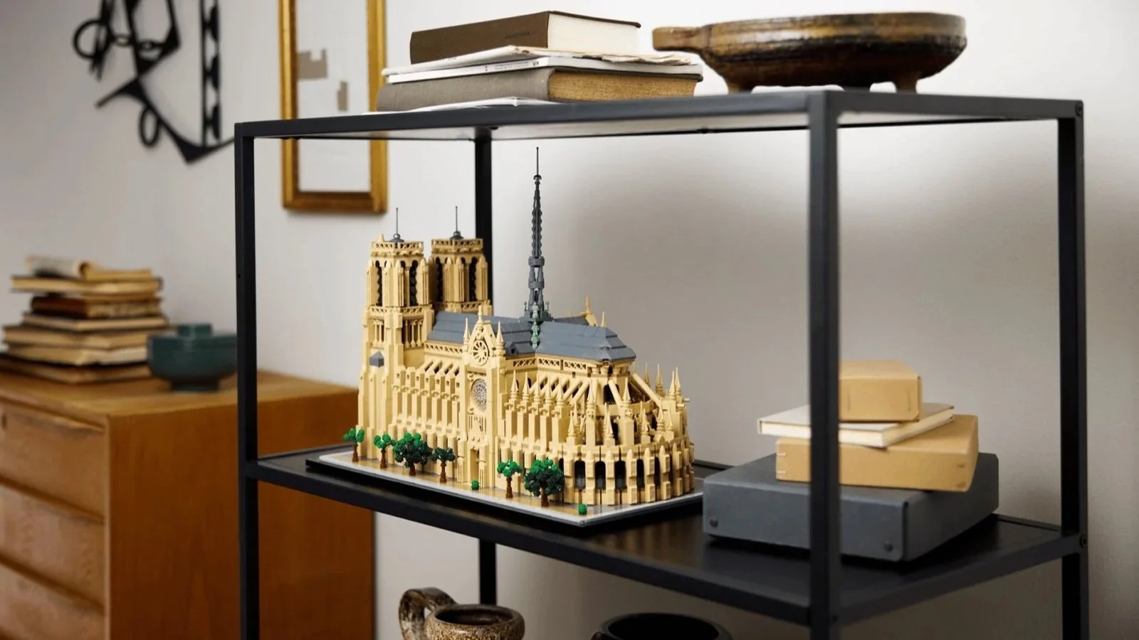 LEGO Notre-Dame de Paris set displayed on a black metal shelf among stacked books and ceramic vases