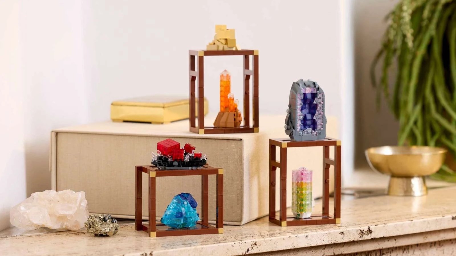 LEGO Mineral Collection crystal builds in brass-accented display stands on a marble mantle, beside a raw quartz cluster, a pyrite chunk, and a small gold box