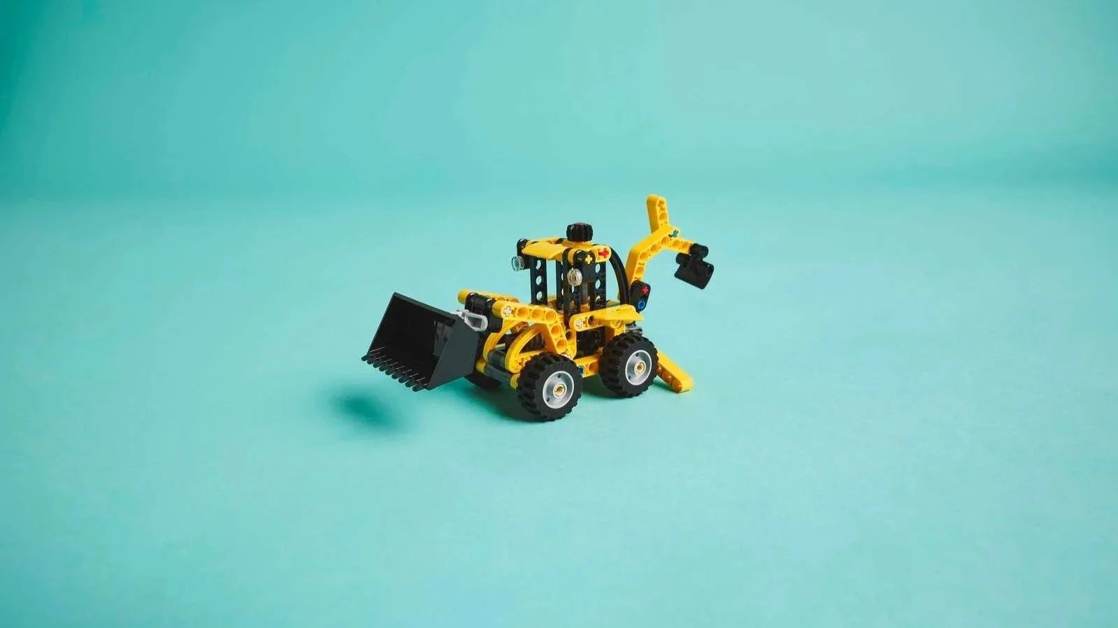 Yellow and black LEGO Technic Backhoe Loader with a front bucket and rear digging arm on a teal background