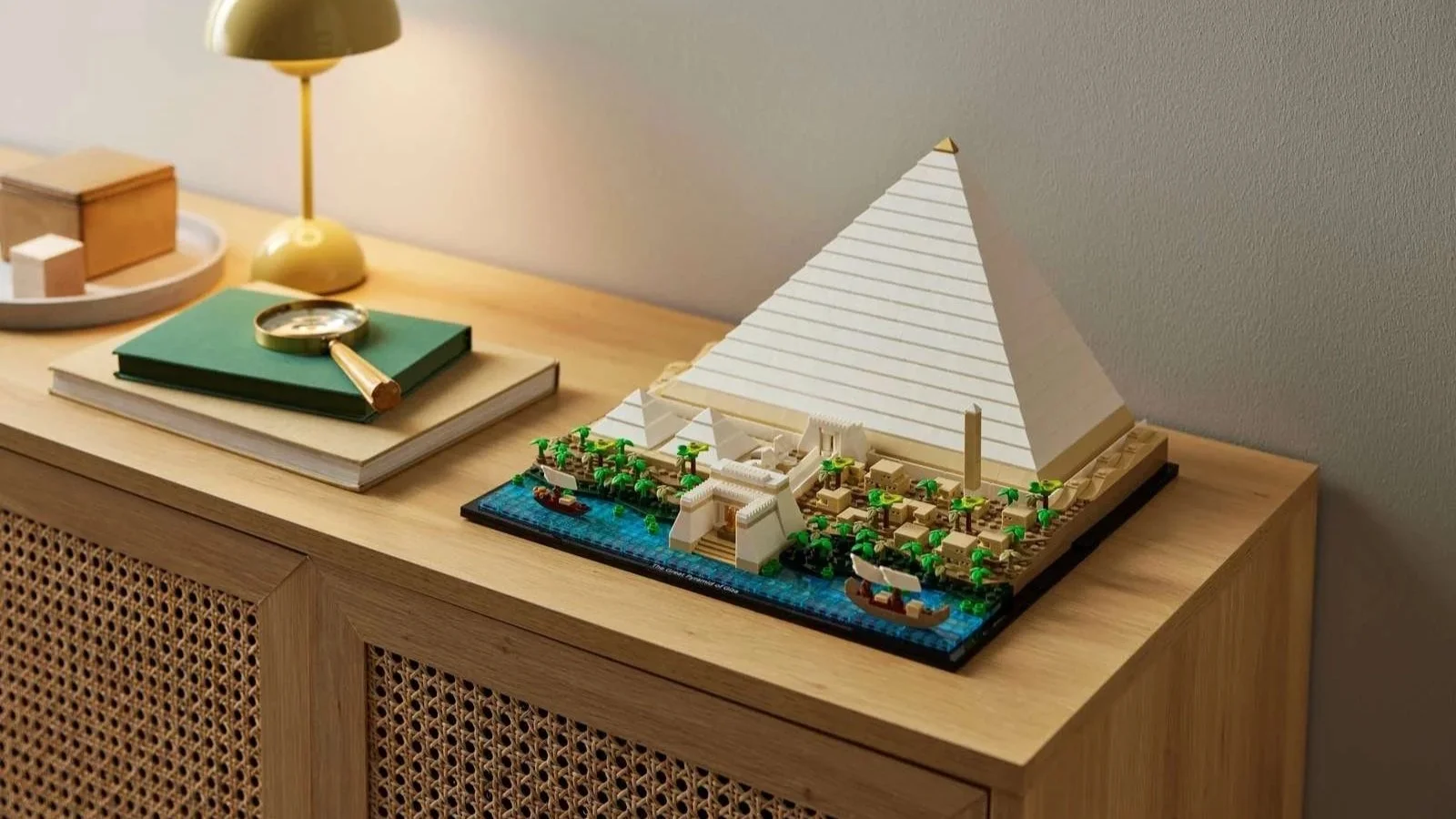 LEGO Great Pyramid of Giza set on a light oak sideboard next to a green book and brass magnifying glass