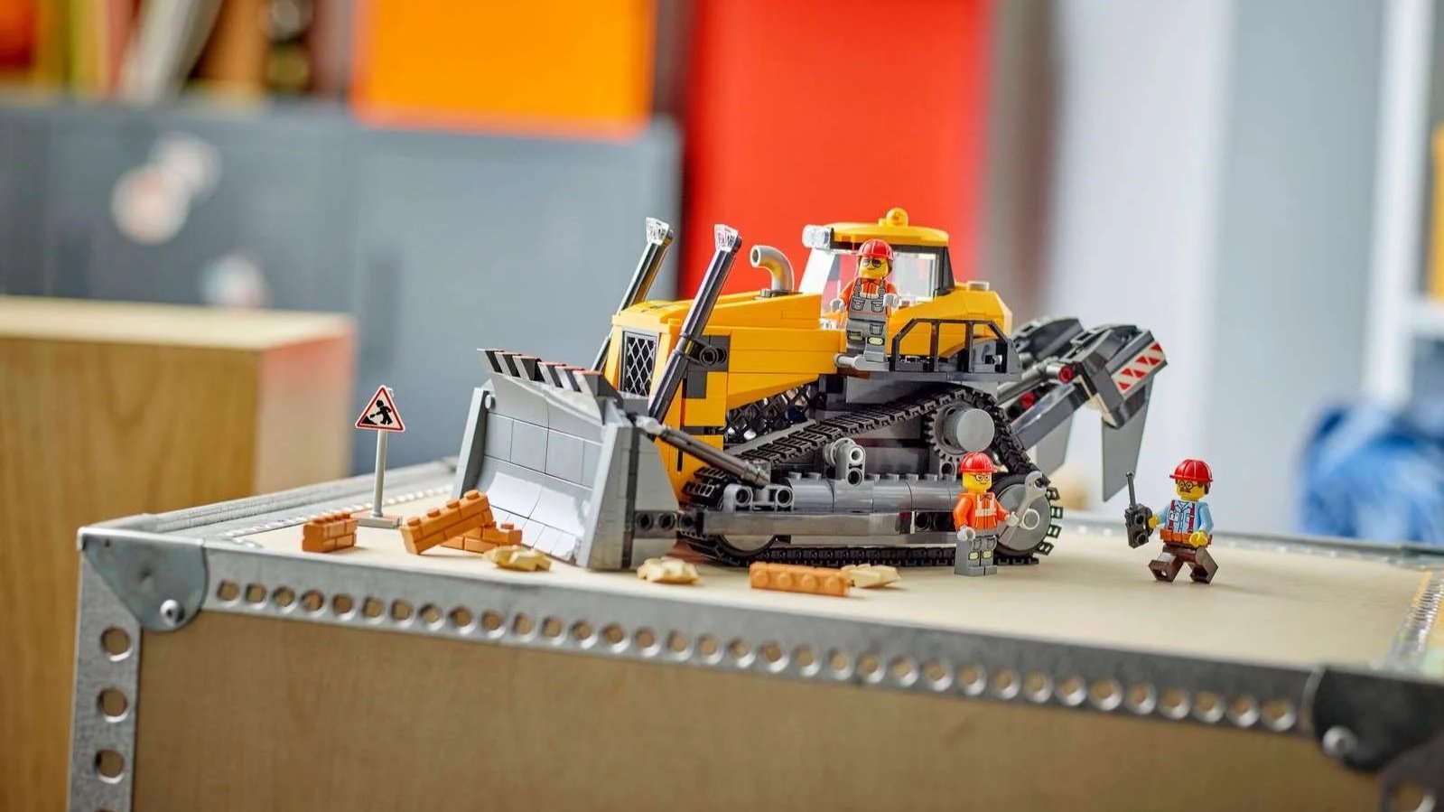 LEGO Yellow Bulldozer set with a gray blade and tracks, three construction minifigures and scattered brick rubble on a metal-cornered shelf