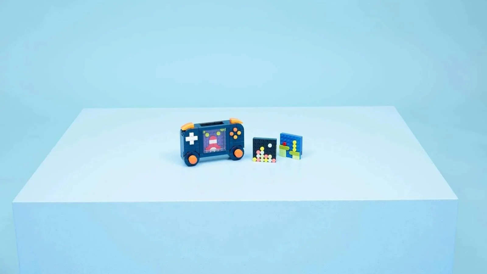 LEGO Retro Gaming Console set in navy blue and orange, staged on a light blue riser next to two pixel art tile builds