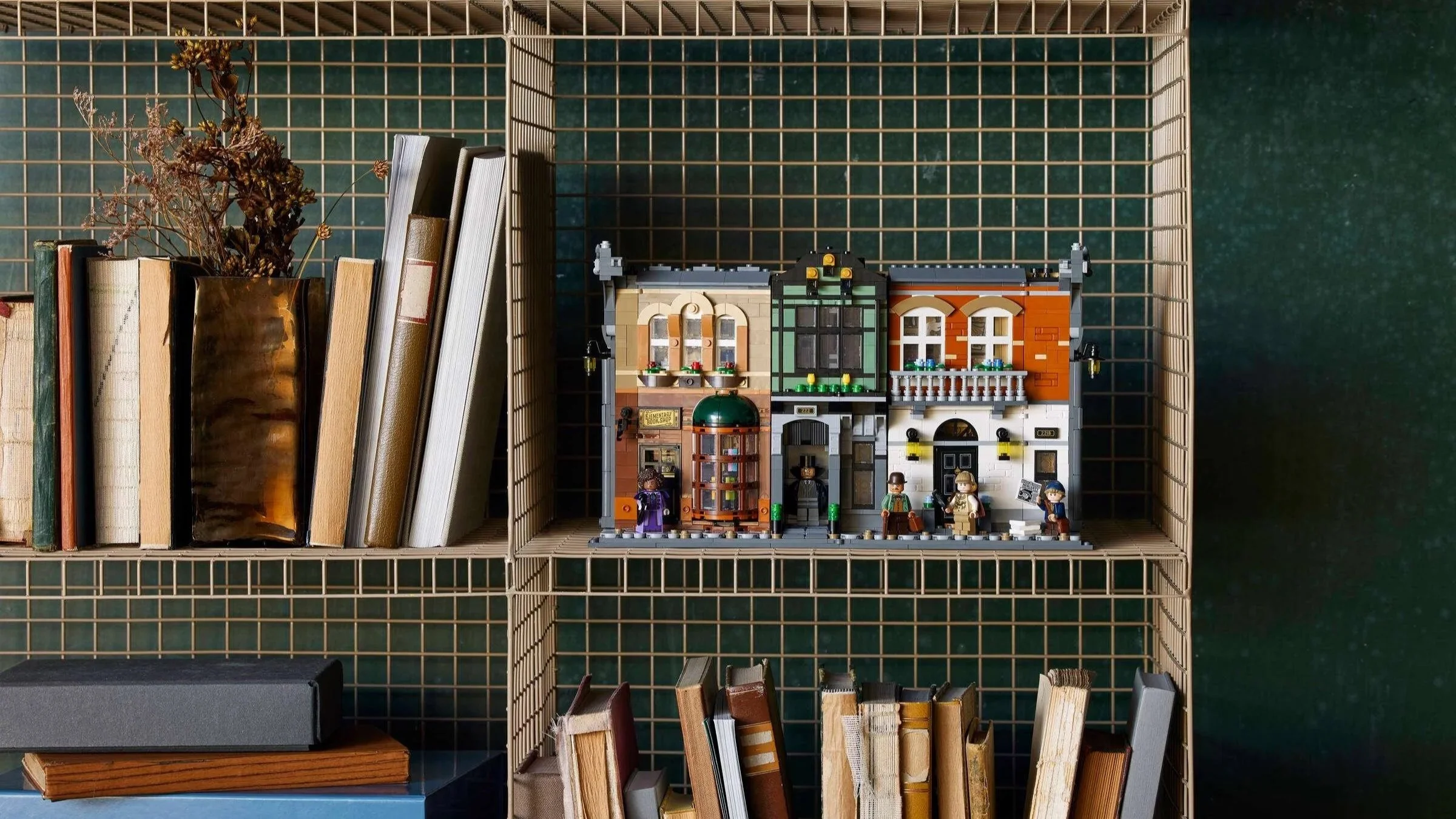 A row of Victorian shop and townhouse facades from the LEGO Sherlock Holmes Book Nook, with detective minifigures out front, displayed on a wire shelf beside dried flowers