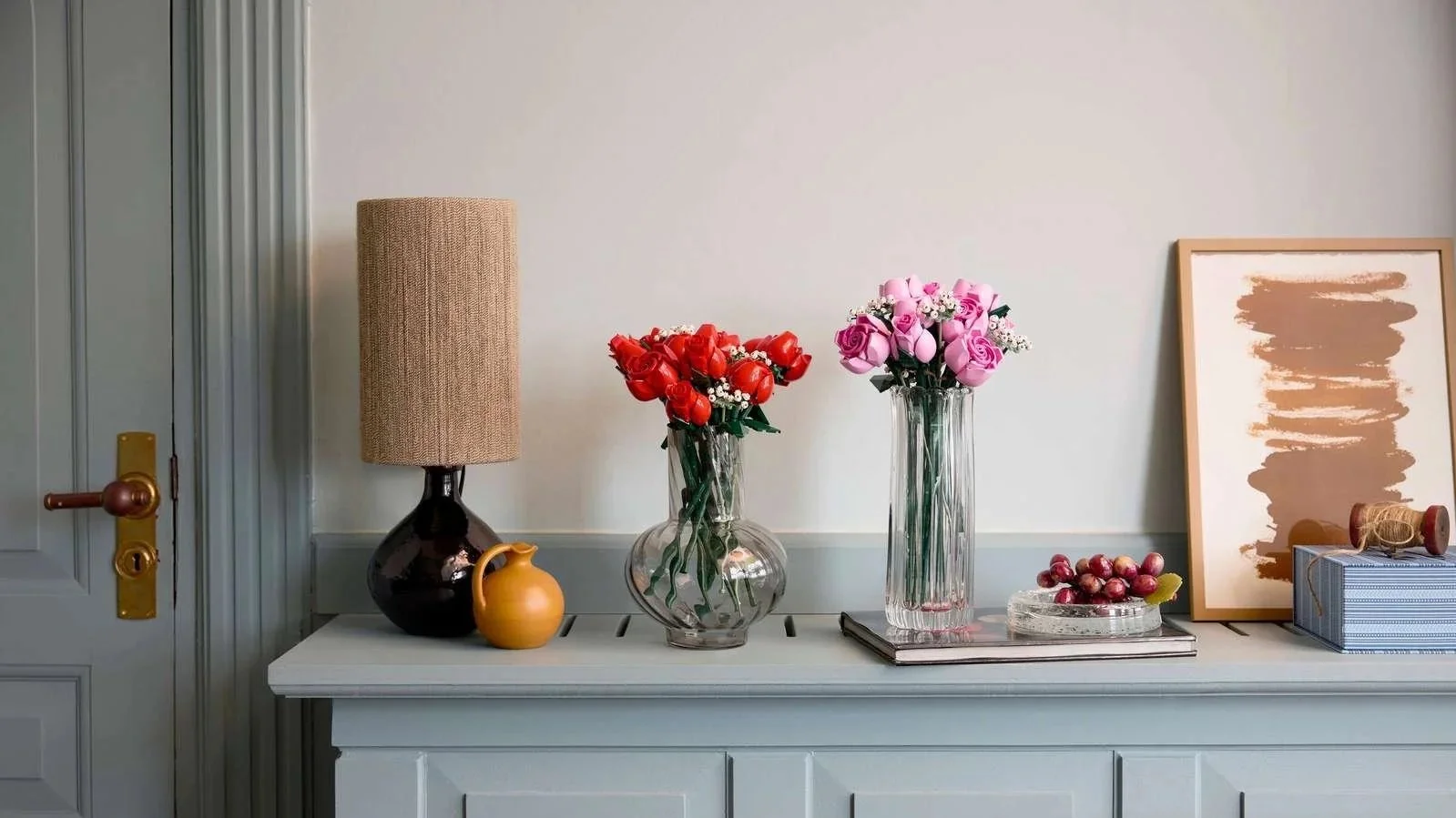 LEGO Bouquet of Roses and Bouquet of Pink Roses side by side in glass vases on a blue-gray sideboard