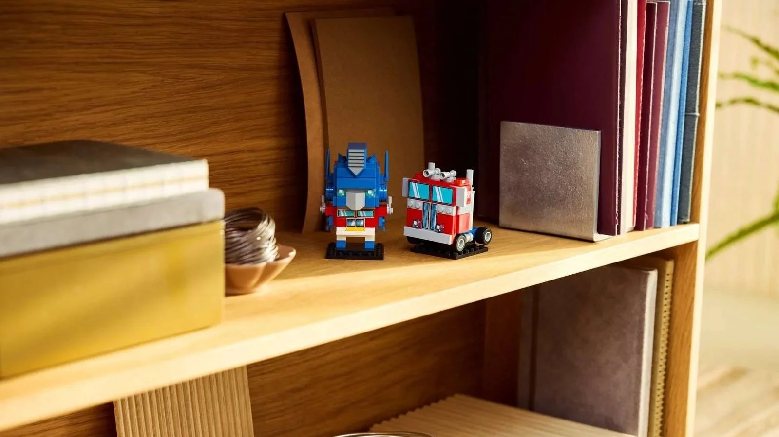 LEGO Optimus Prime robot figure and red truck on a wooden bookshelf next to books