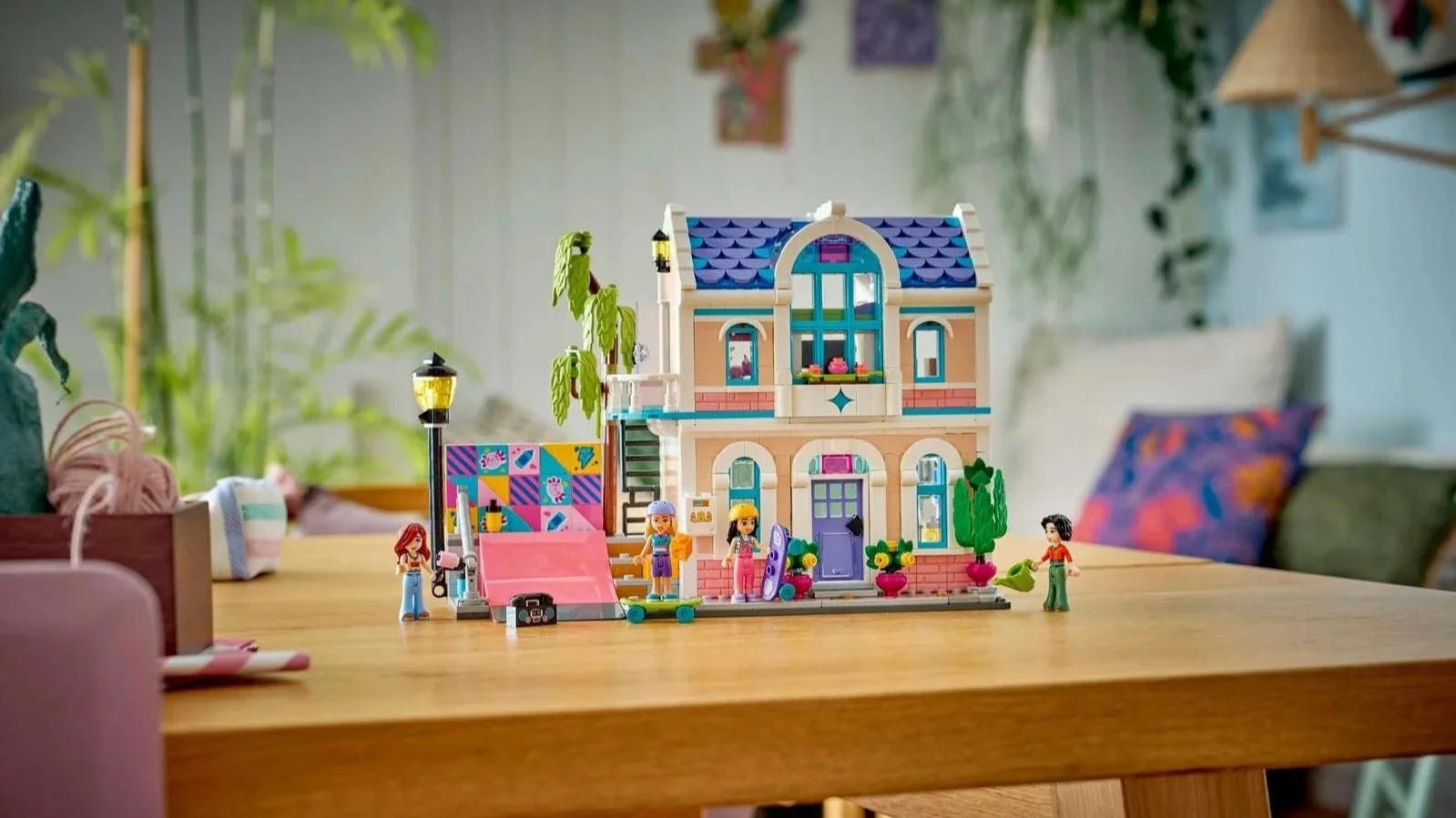 LEGO Liann's Family House set on a wooden table, a peach two-story house with a blue scalloped roof and purple door, beside a pink skate ramp and four figures