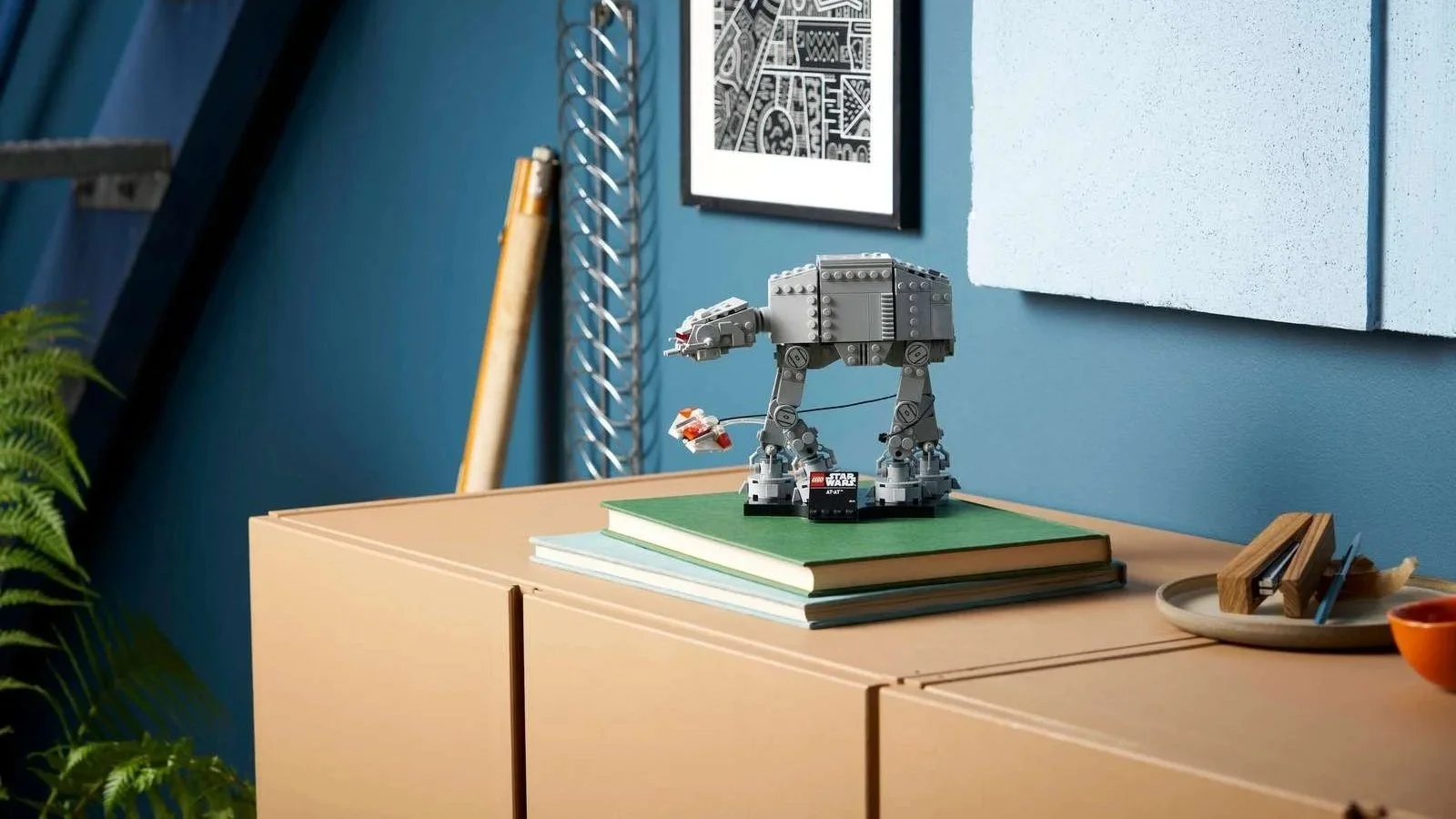 LEGO Star Wars AT-AT posed on stacked books on a sideboard, with a mini snowspeeder circling its legs