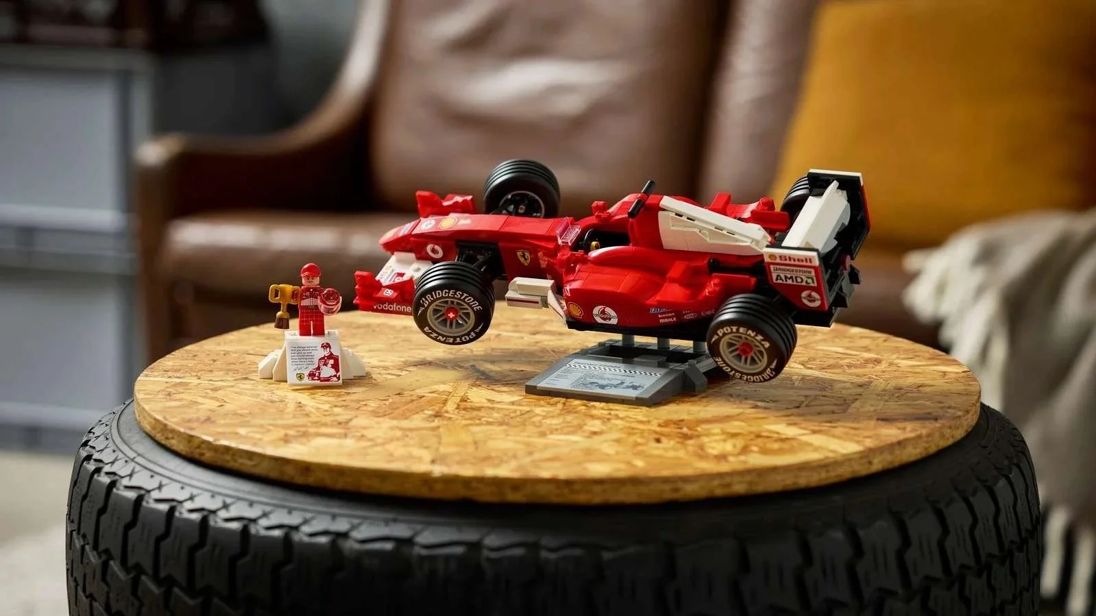 Red LEGO Ferrari F2004 race car on a display stand next to a Michael Schumacher minifigure holding a trophy, on a round wooden tire table