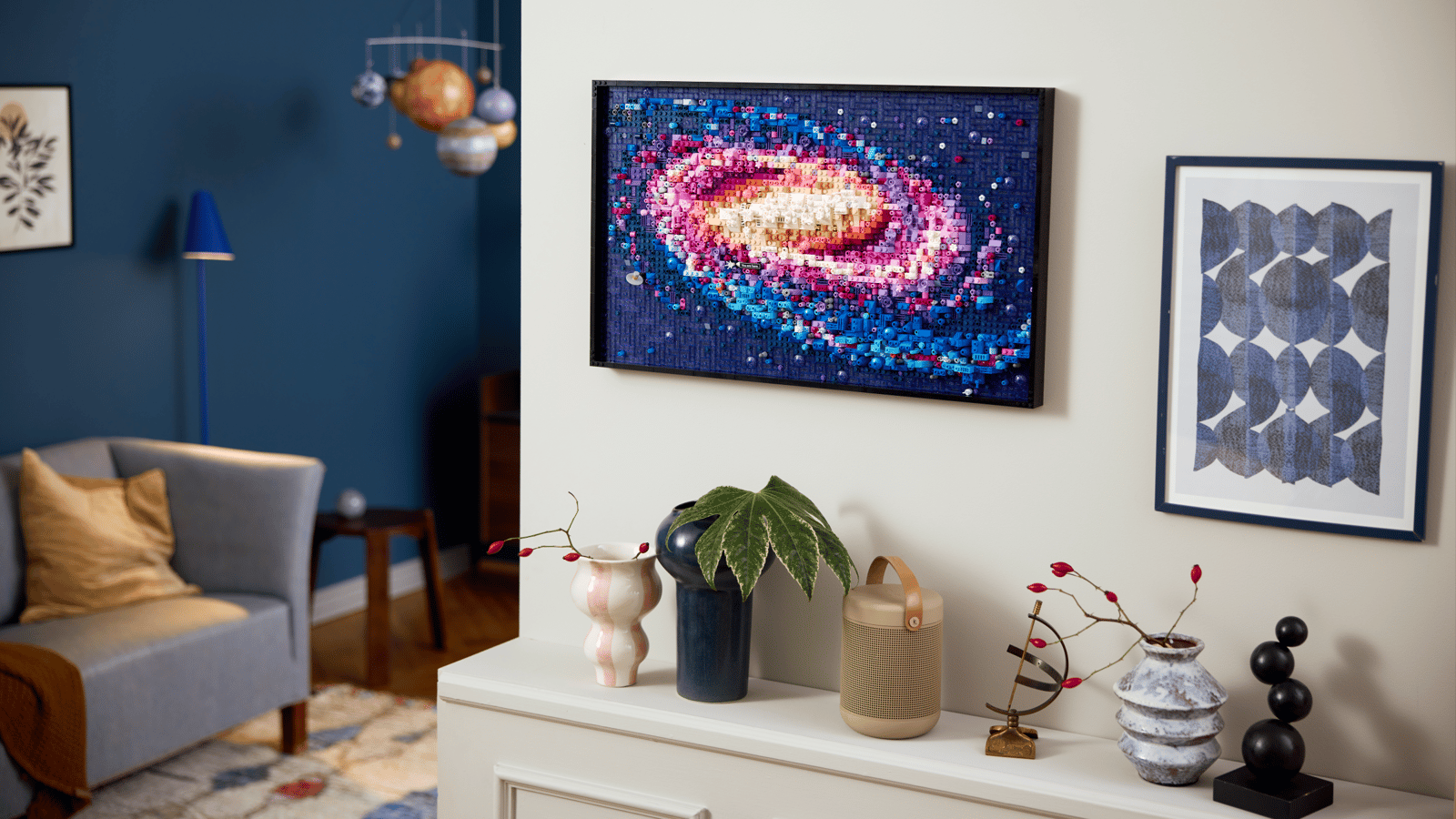 LEGO The Milky Way Galaxy set hanging on a white wall above a styled sideboard, with a planet mobile nearby