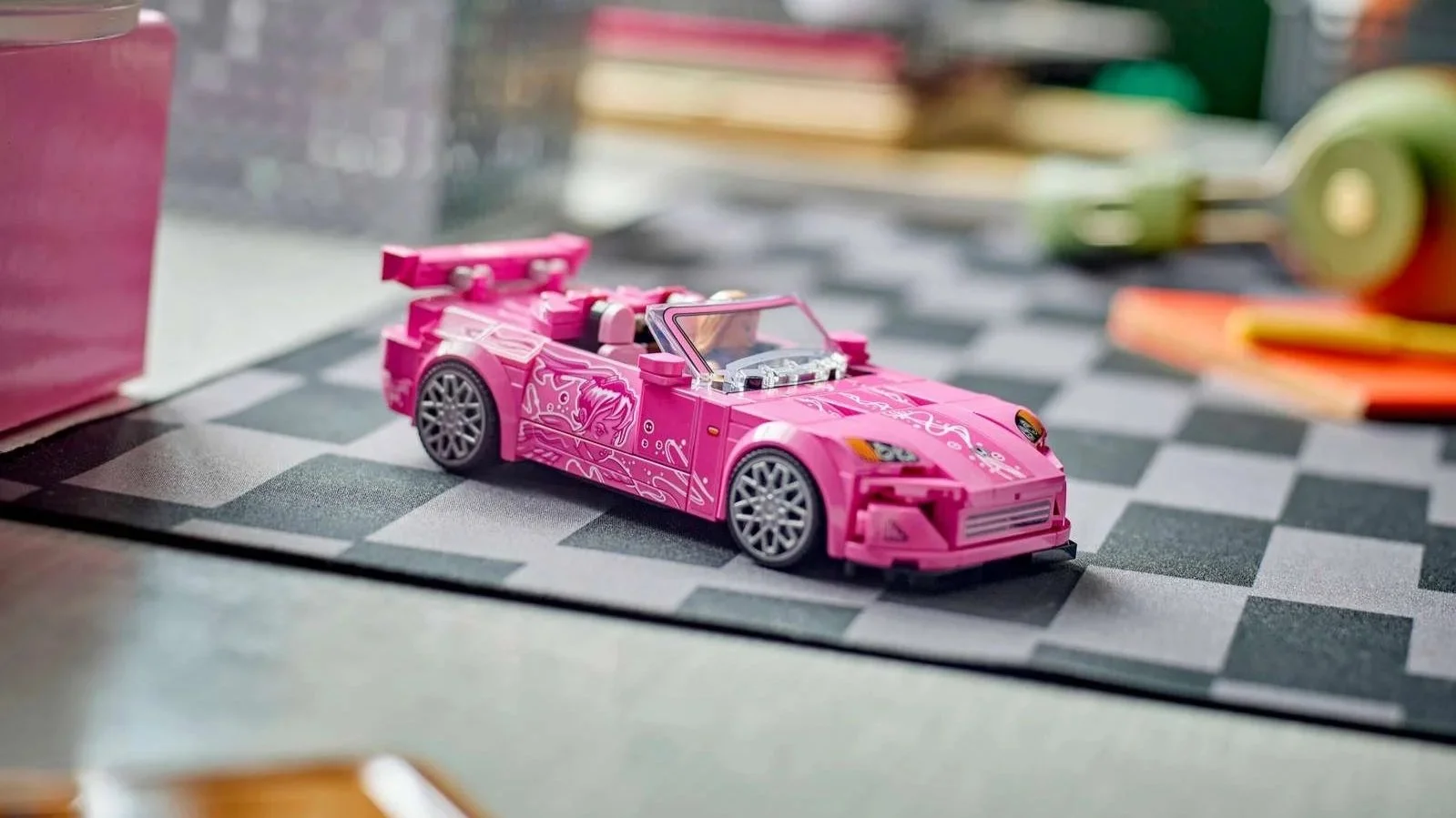 Pink LEGO 2 Fast 2 Furious Honda S2000 with white graphic decals and a minifigure driver on a checkered desk mat