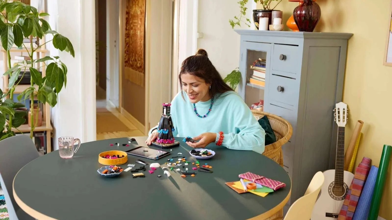 Woman smiling while building the LEGO La Catrina set, with sorted pieces and a tablet showing instructions nearby