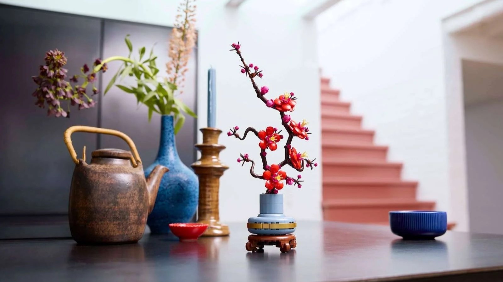 LEGO Plum Blossom set with red flowers on a dark counter next to a teapot, coral stairs behind