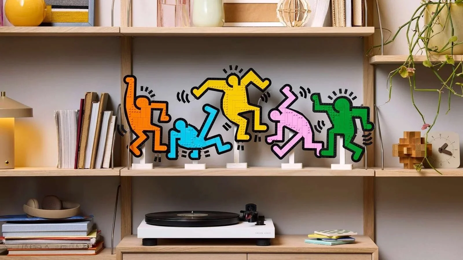 LEGO Keith Haring Dancing Figures set in five colors on a wooden shelf above a record player