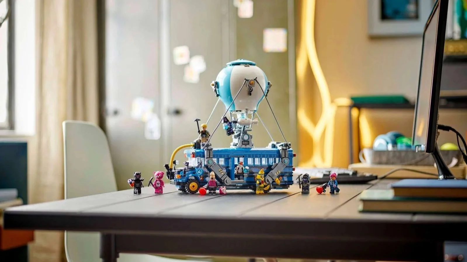 Fortnite Battle Bus LEGO set, a blue bus with a hot air balloon on top and minifigures posed around it on a dark desk