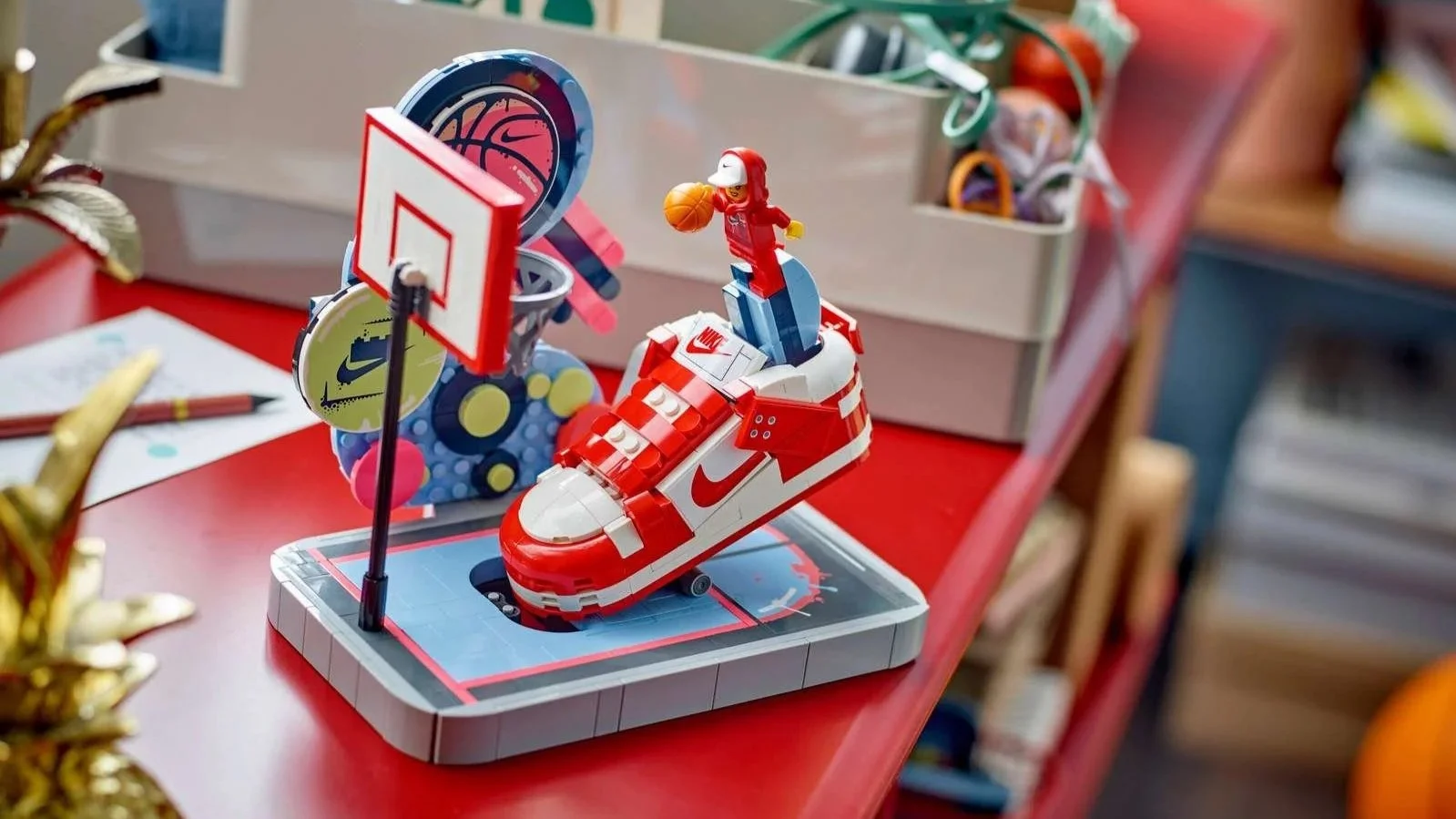 LEGO Nike Dunk Trickshot set with a red and white sneaker, a hoop and a minifigure dribbling a basketball, on a red desk
