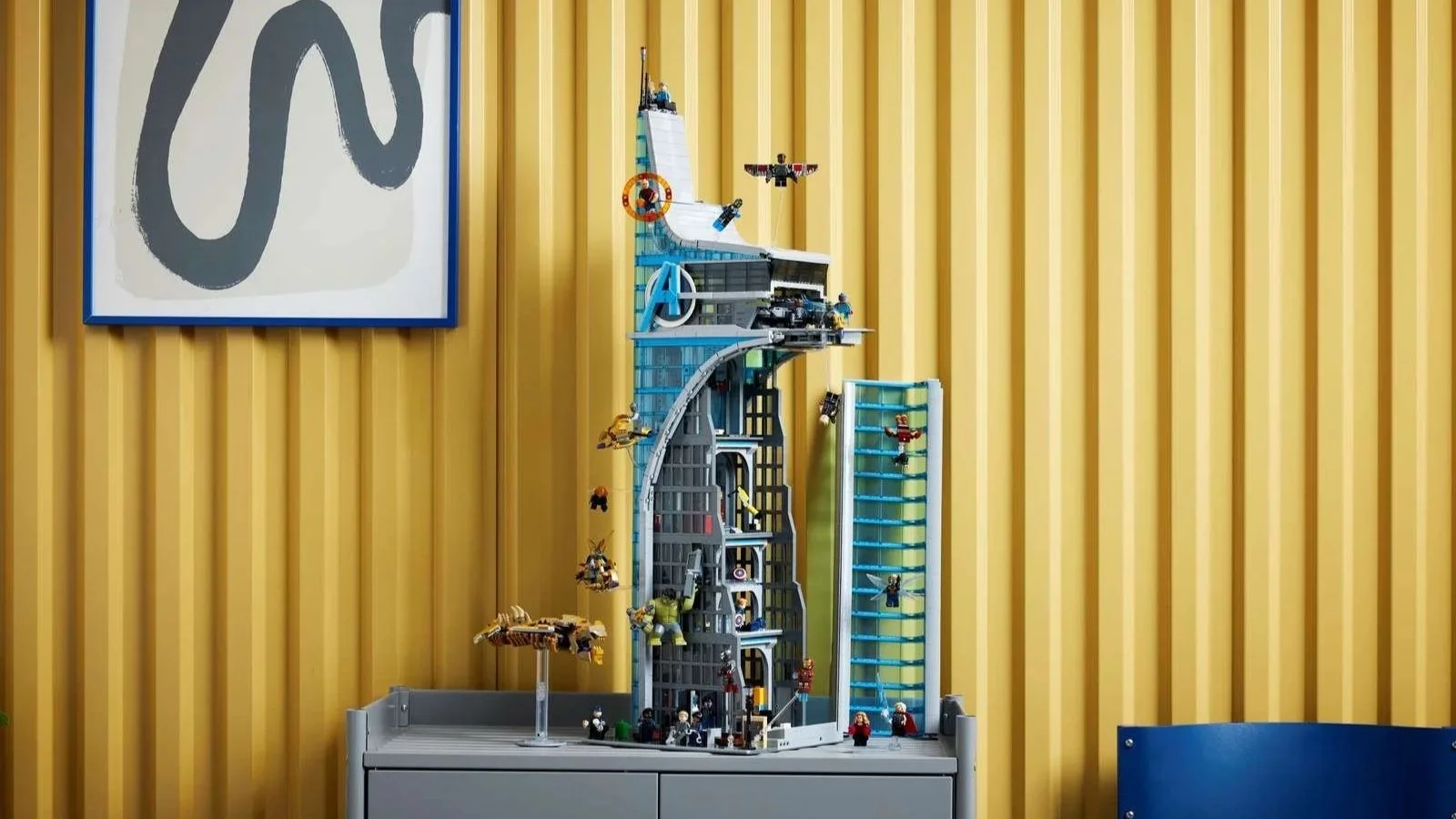 LEGO Marvel Avengers Tower set with flying superhero minifigures displayed on a gray cabinet against a yellow wall