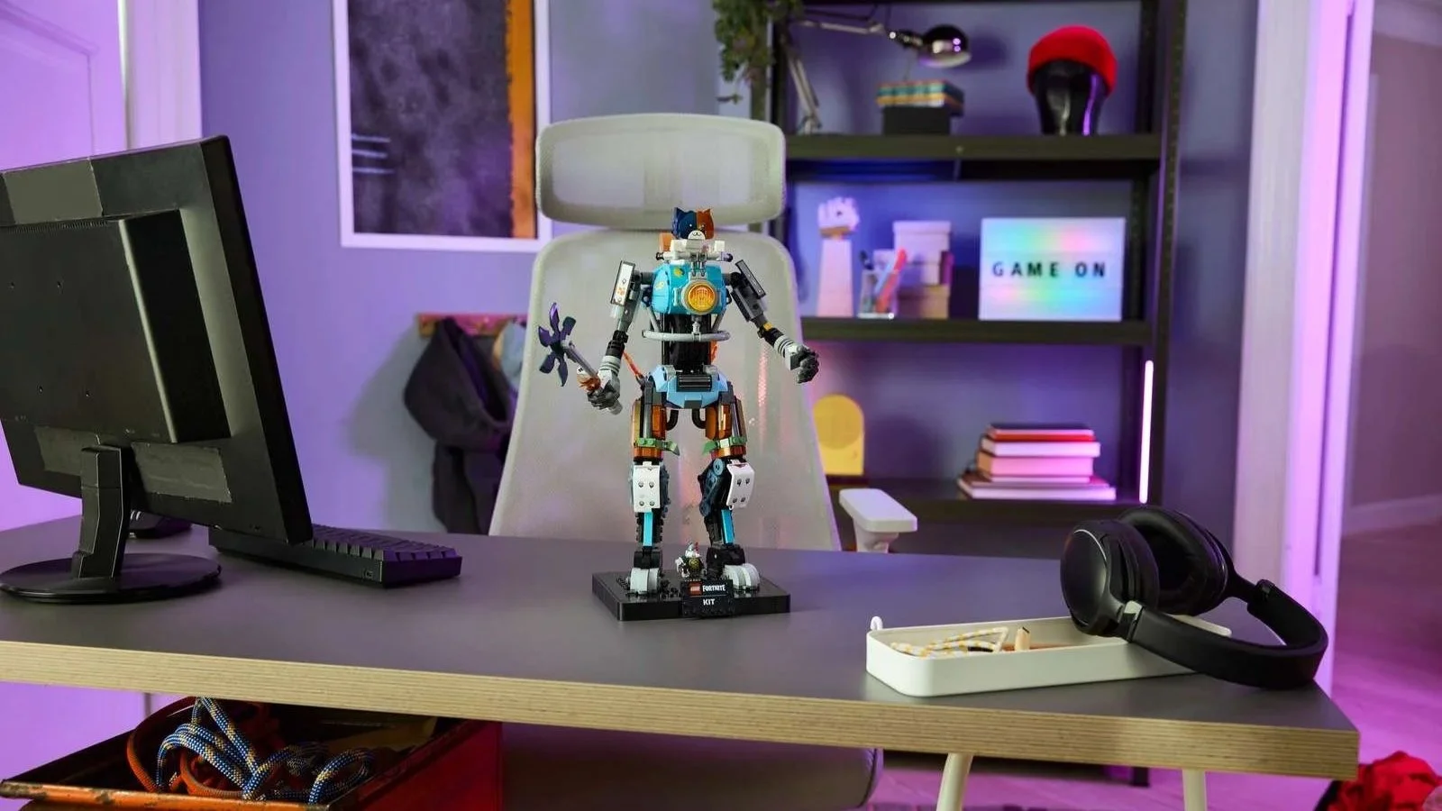 LEGO Fortnite KIT figure holding its weapon on a desk beside a monitor and headphones under purple gaming room lighting