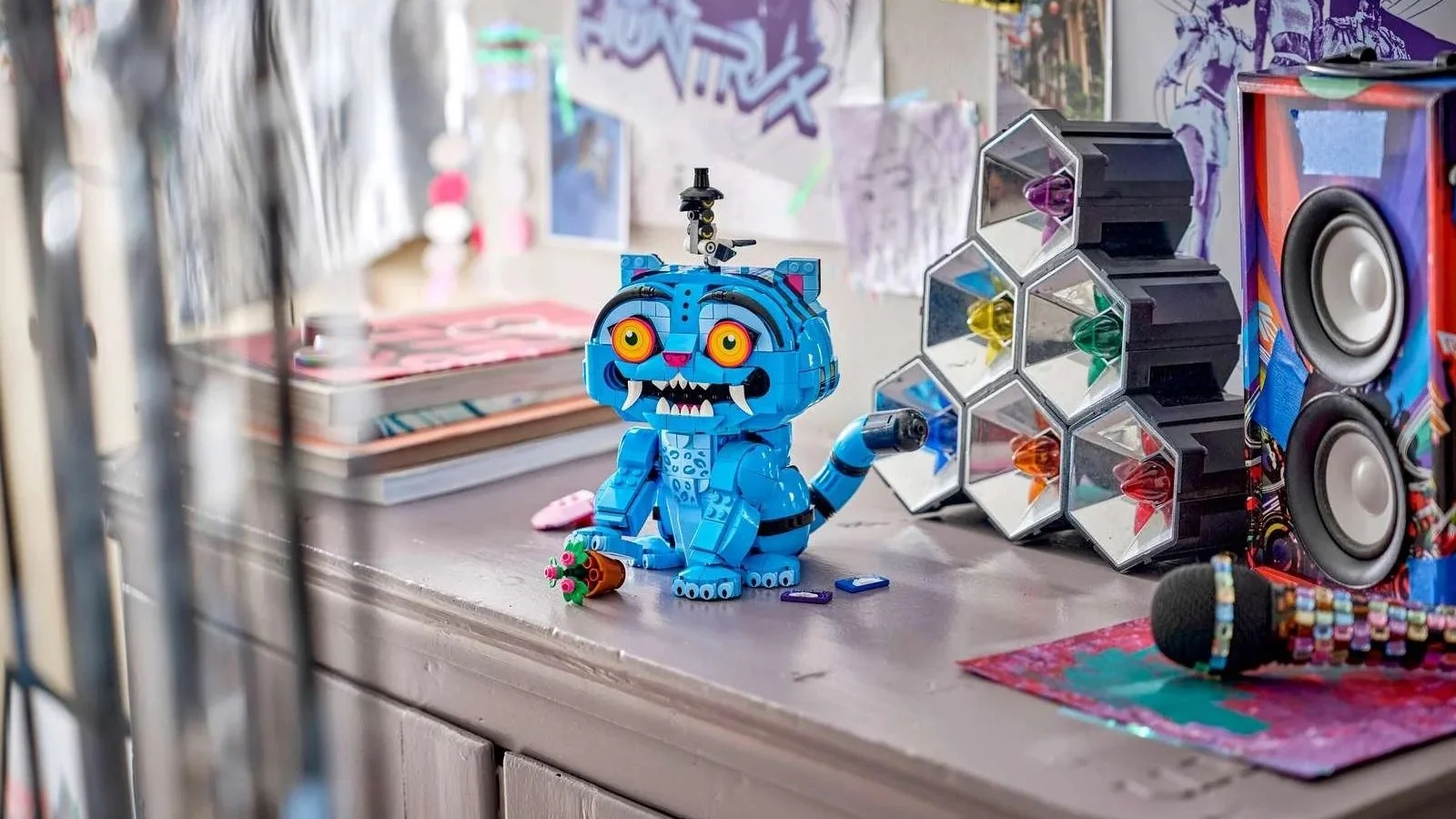 LEGO Derpy Tiger figure in bright blue with orange eyes and fangs, Sussie Bird perched on its head, on a dresser beside a speaker