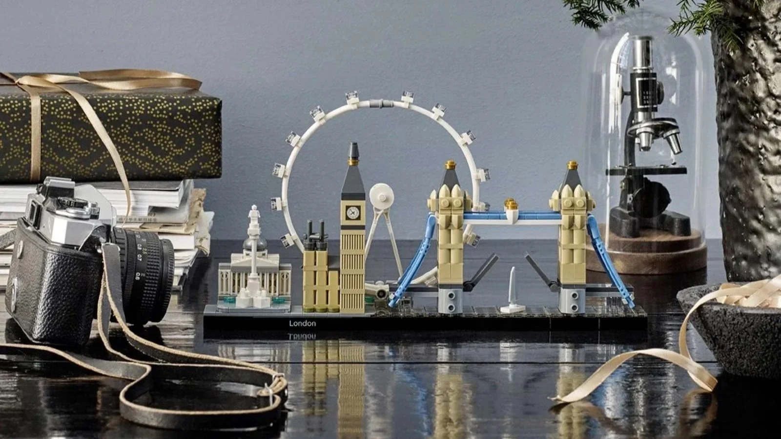 LEGO London skyline set reflected in a glossy black table beside a vintage camera and wrapped gift