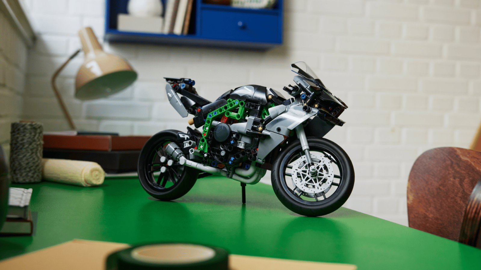 LEGO Kawasaki Ninja H2R motorcycle in black, grey and green on a green desk in front of a white brick wall