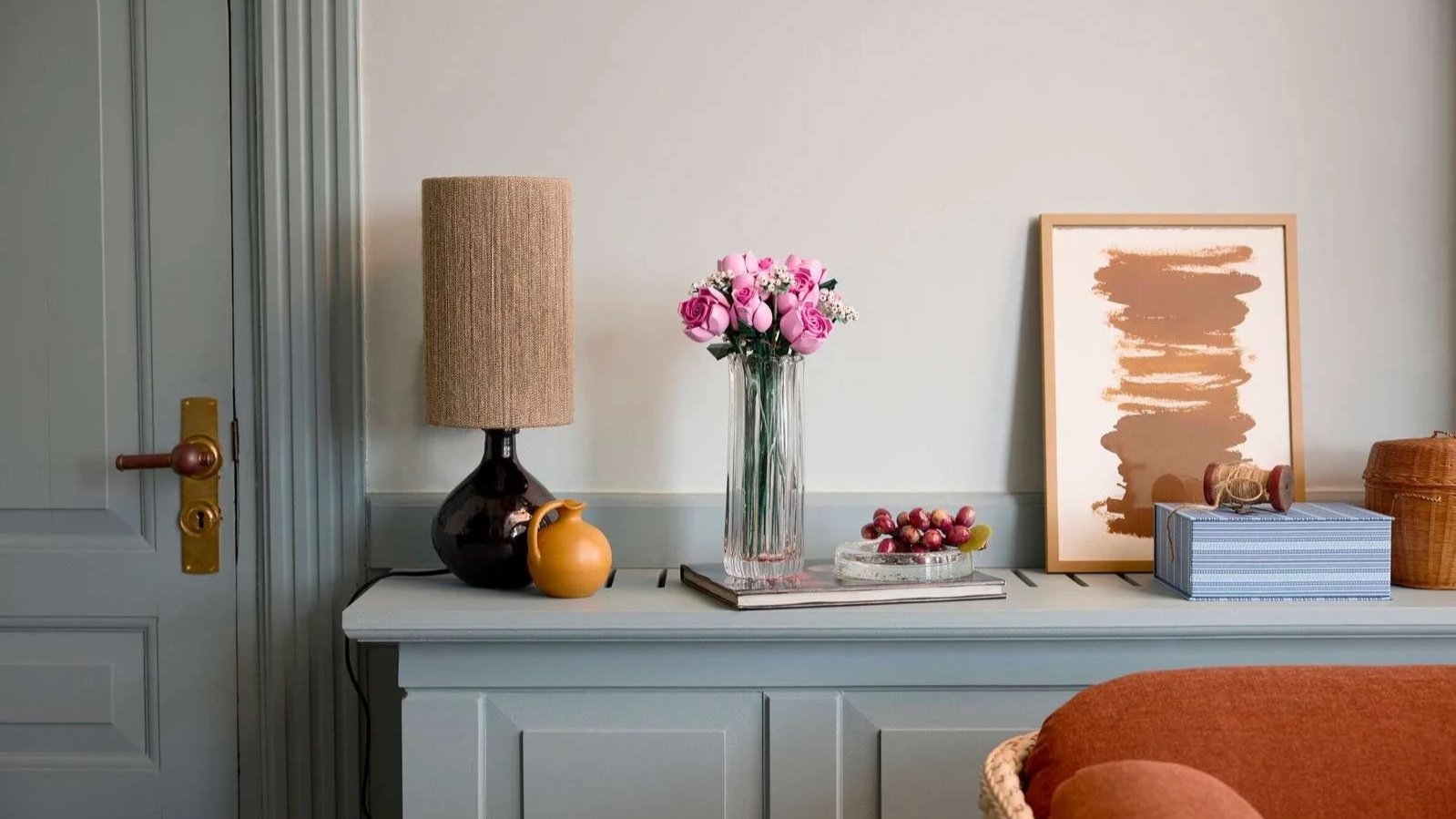 LEGO Bouquet of Pink Roses set in a fluted glass vase on a pale blue sideboard beside a table lamp