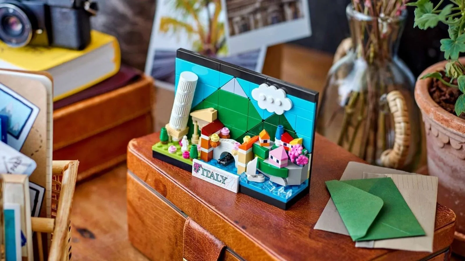 LEGO Italy Postcard set on a brown leather box, showing the Leaning Tower of Pisa, green hills and colorful seaside houses beside a vintage camera