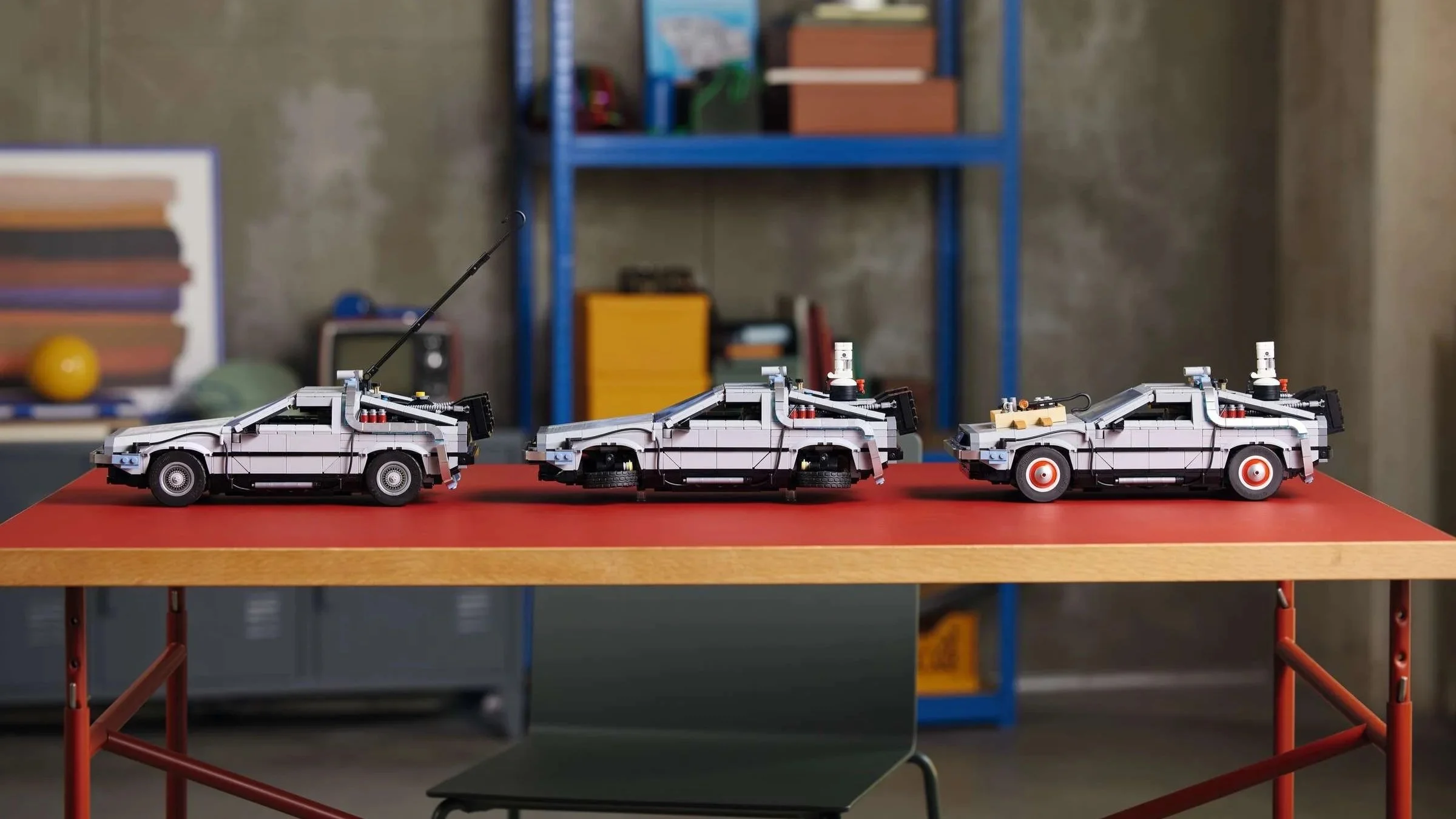 All three DeLorean versions of the LEGO Back to the Future Time Machine set lined up side by side on a red worktable.