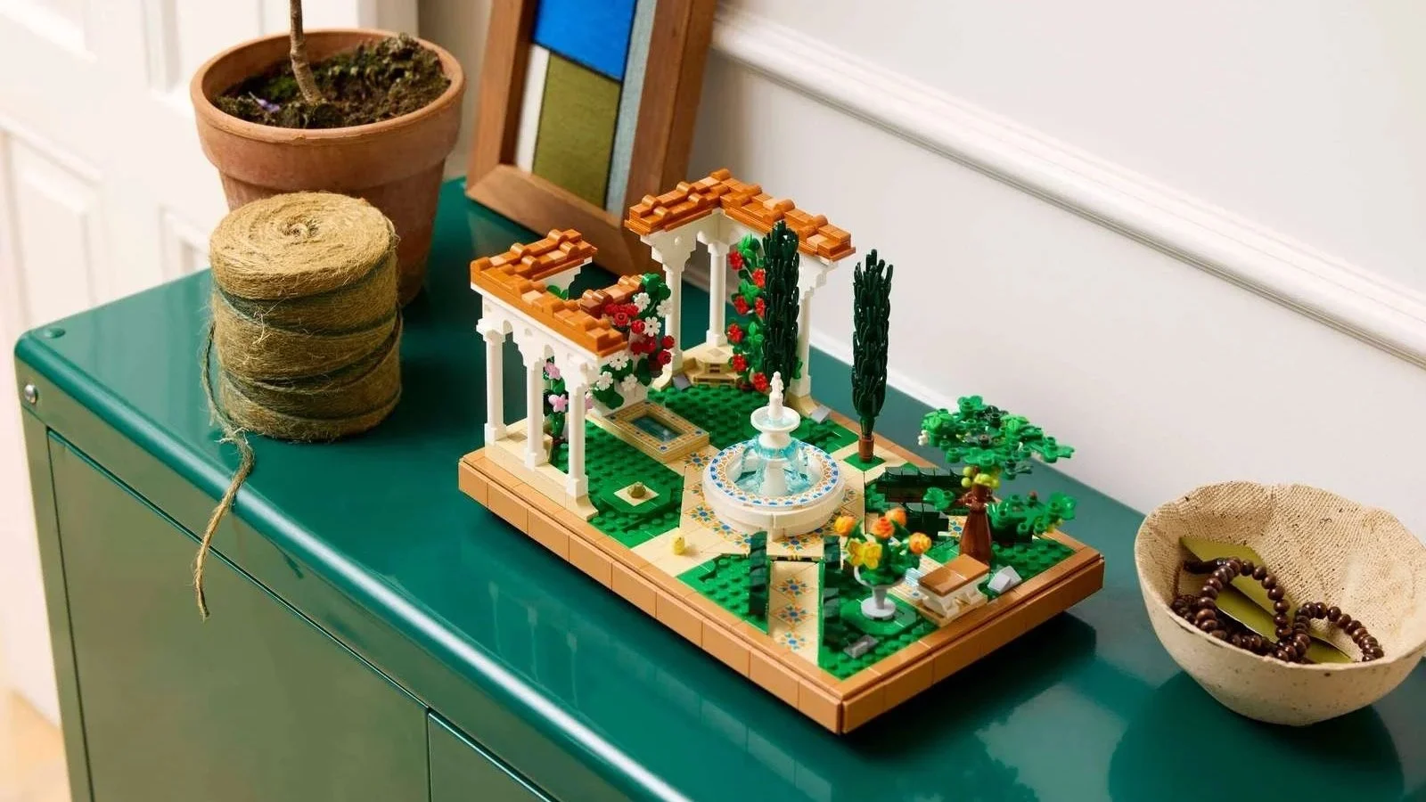 LEGO Fountain Garden set with columns and cypress trees on a green cabinet beside a potted plant