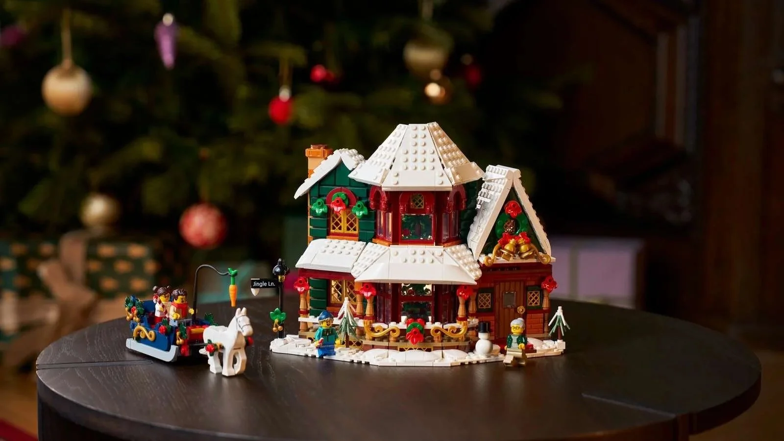 LEGO Holiday House with snow-covered roofs and red and green walls, plus a sleigh and white horse, in front of a Christmas tree